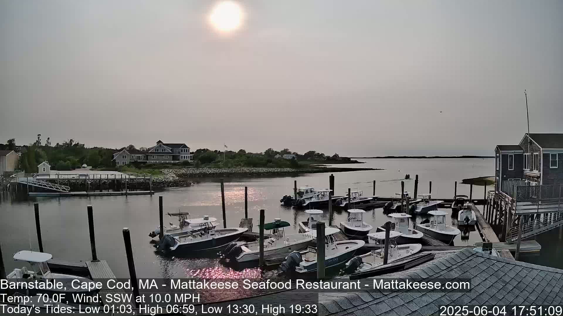 A hazy sunset illuminates a calm harbor filled with numerous docked motorboats near a shoreline with houses.