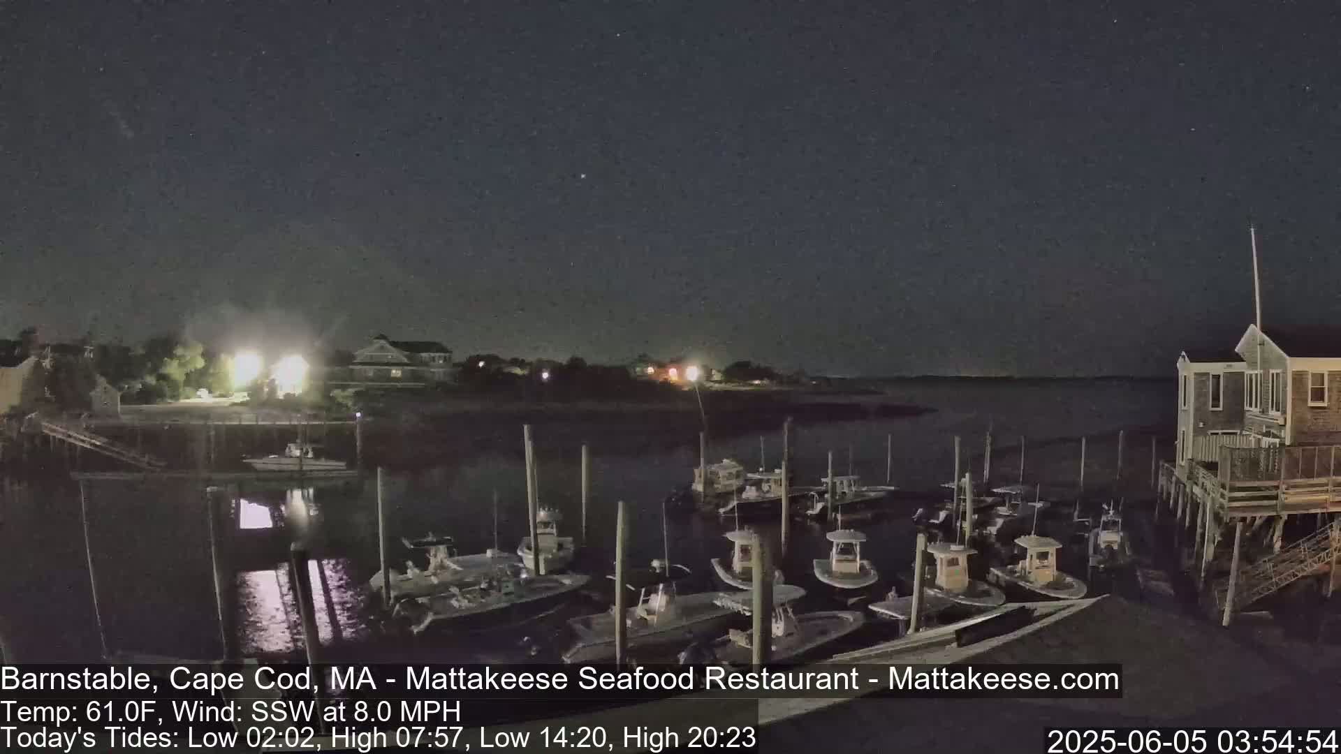 Under a dark night sky, numerous boats are docked at a marina next to a building on stilts.