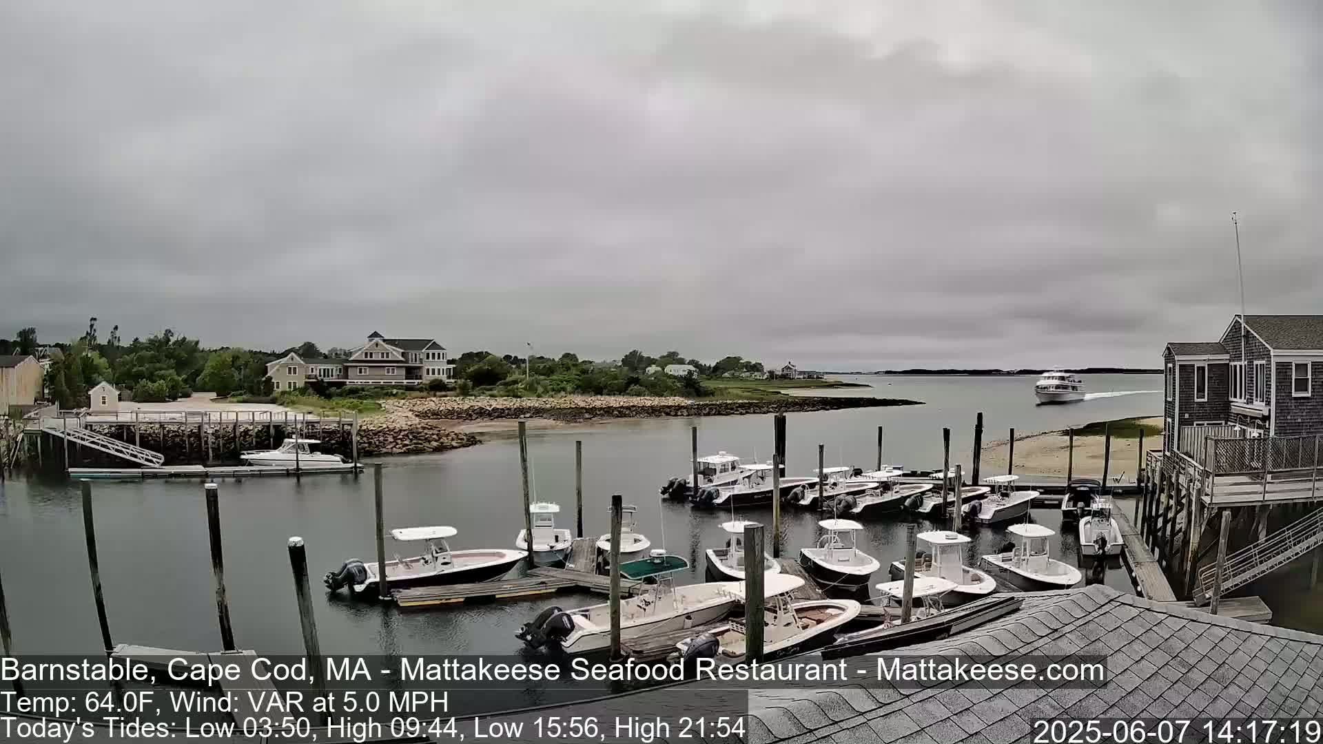 A marina filled with numerous small motorboats is seen under an overcast sky, with a larger boat visible in the distance.