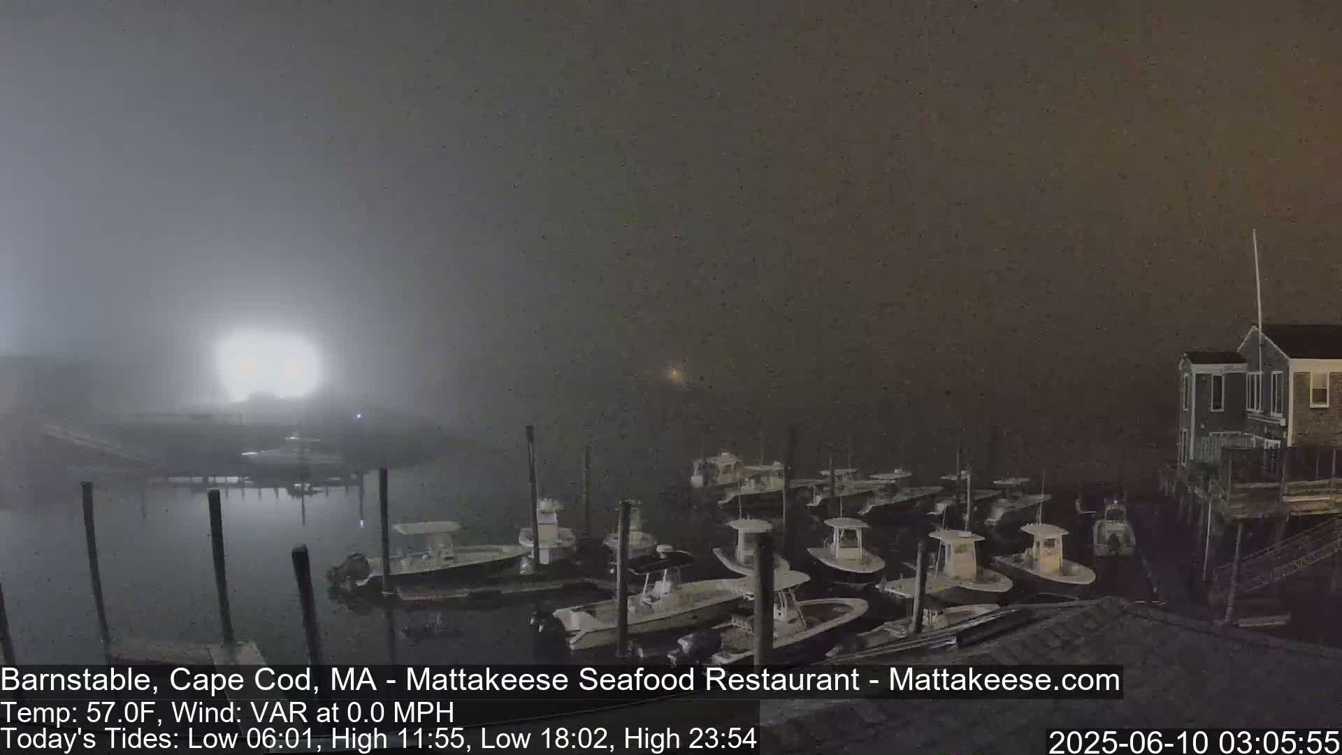 A foggy night scene shows a harbor filled with numerous small boats docked at piers, with a building visible in the upper right corner.