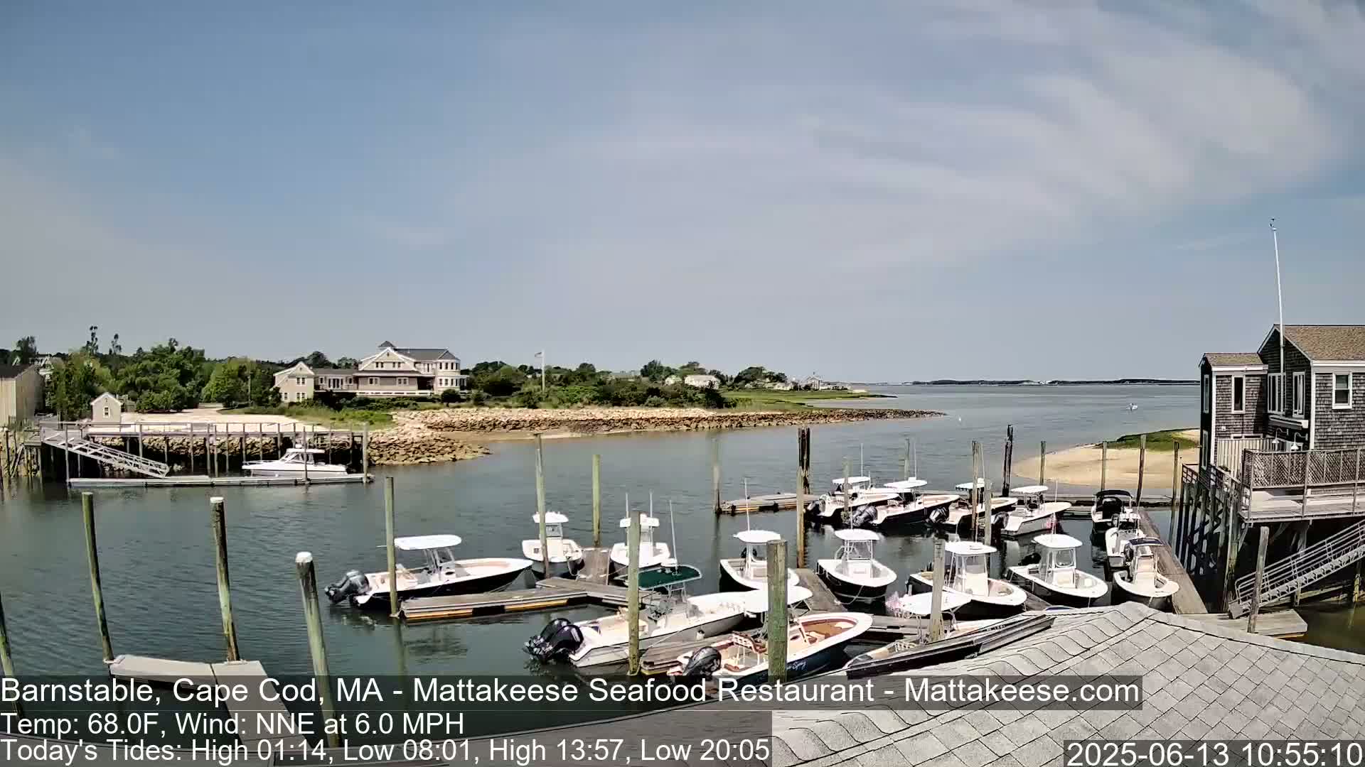 A sunny day shows a harbor filled with docked motorboats, with houses and waterfront structures visible in the background.
