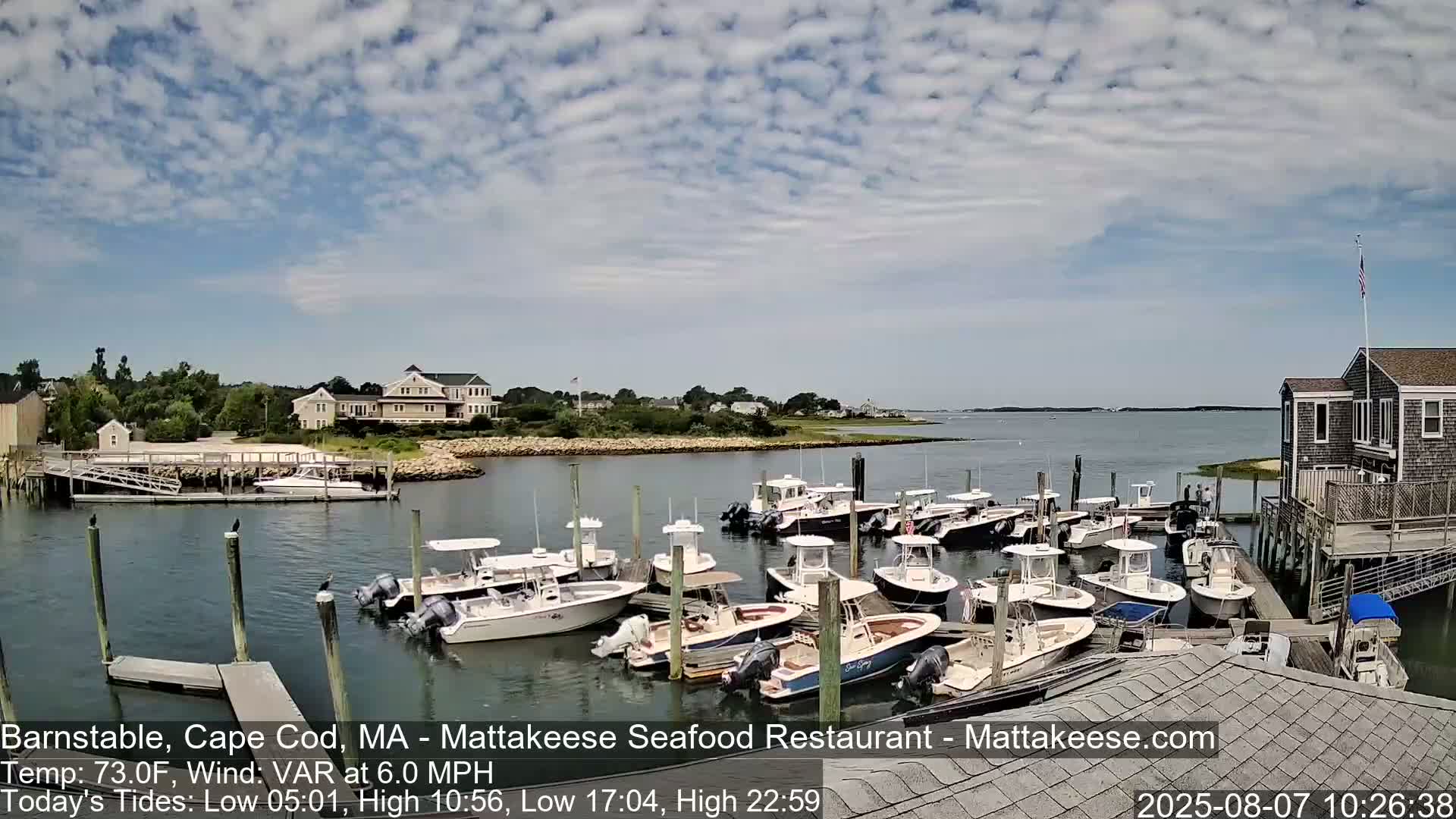 A partly cloudy day shows many small motorboats docked at a waterfront location with a building and calm water.