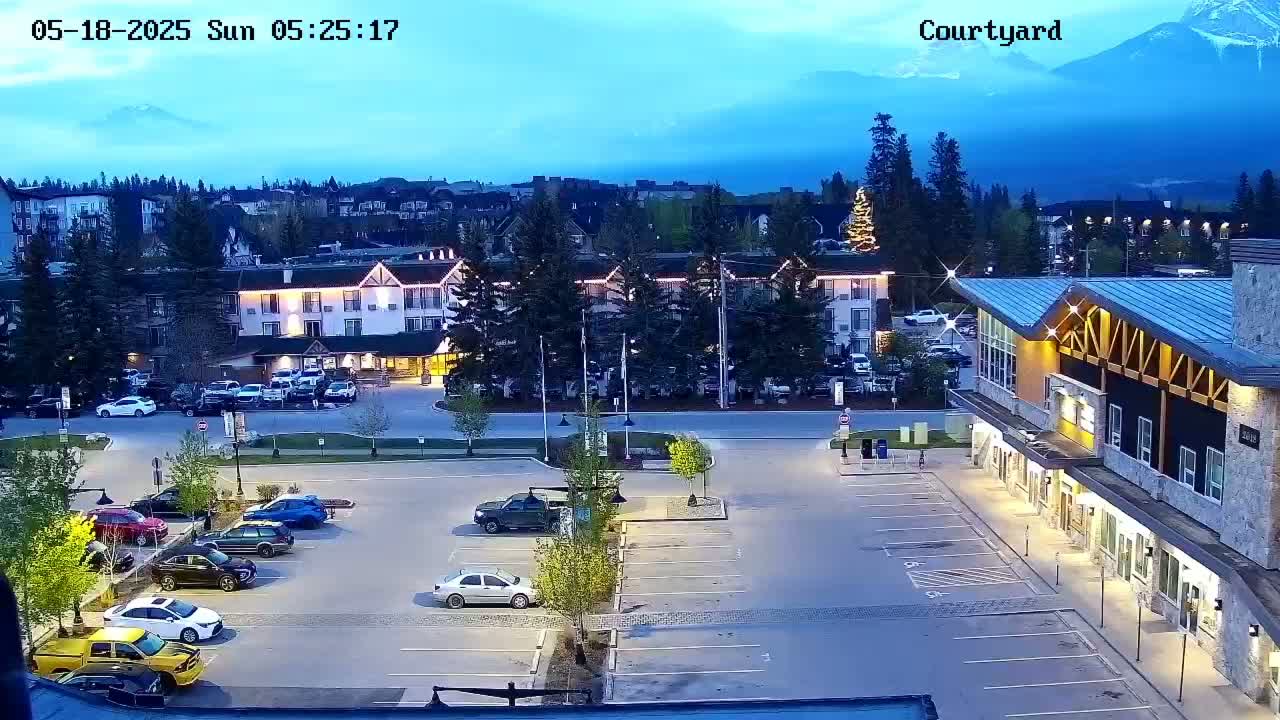 A twilight view of a parking lot and buildings, with mountains in the distance under a clear, dark blue sky.