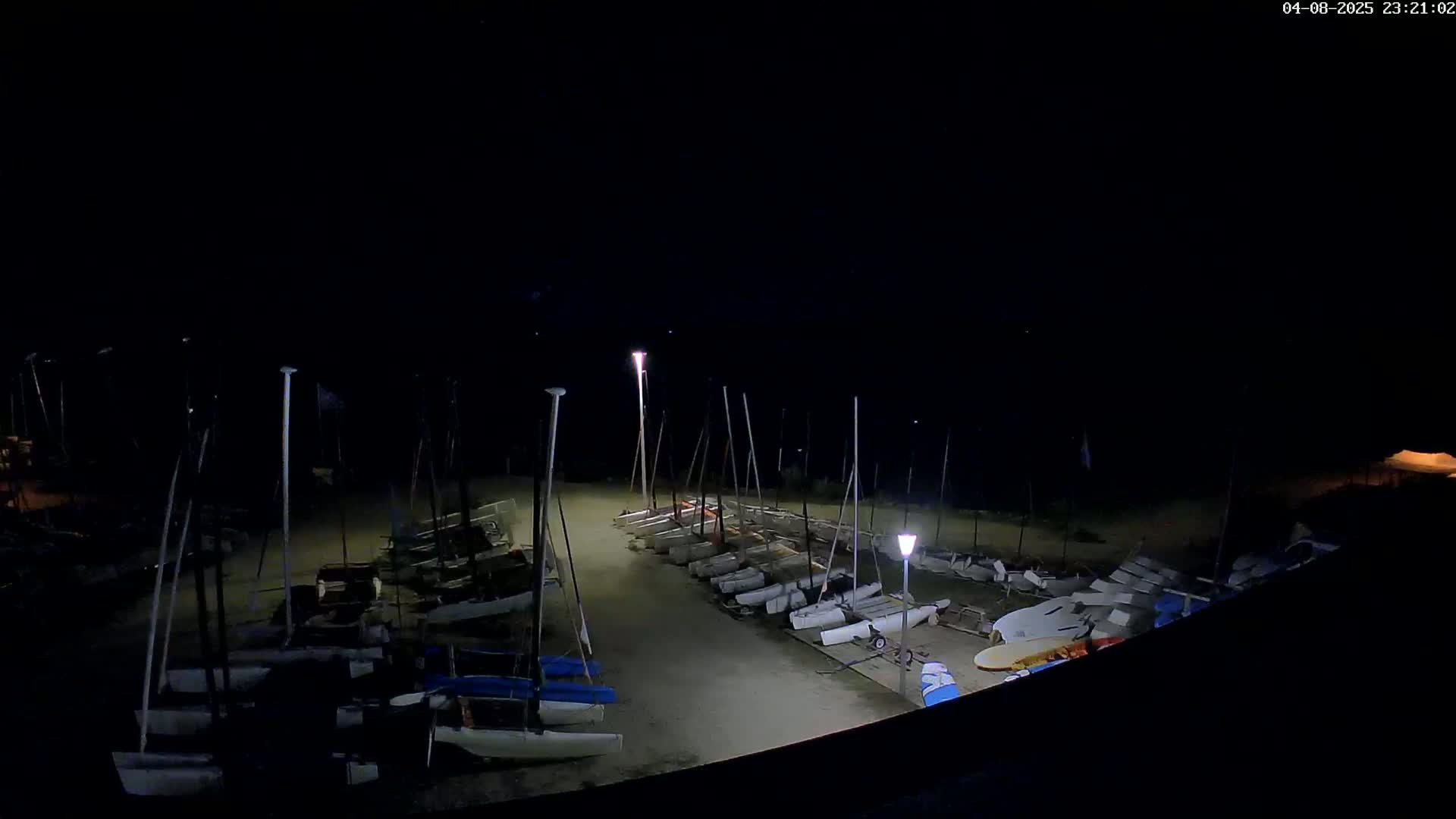 Many sailboats are parked on a sandy area at night under dimly lit conditions.