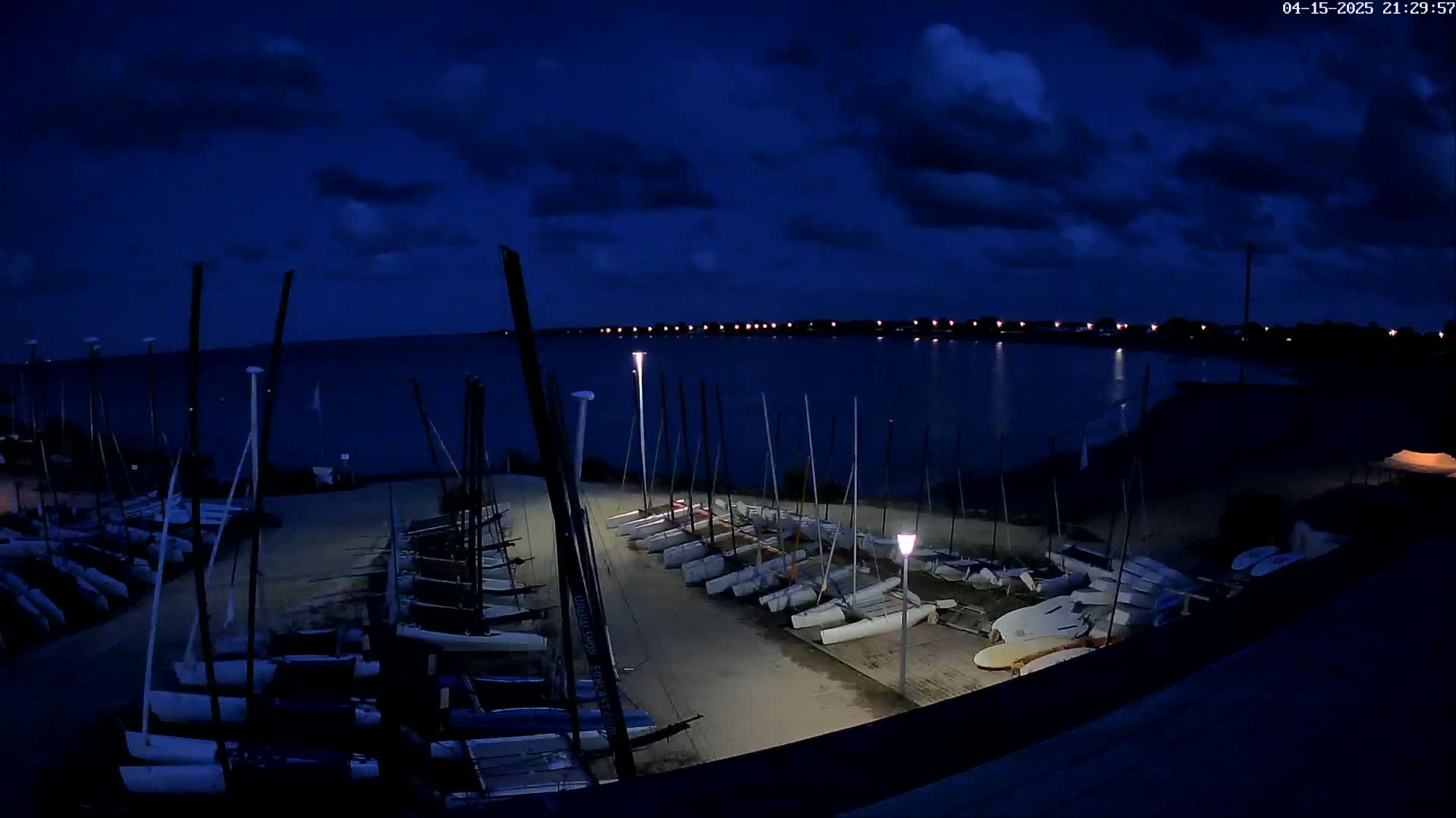 Many sailboats are docked at a waterfront at night under a dark, cloudy sky.