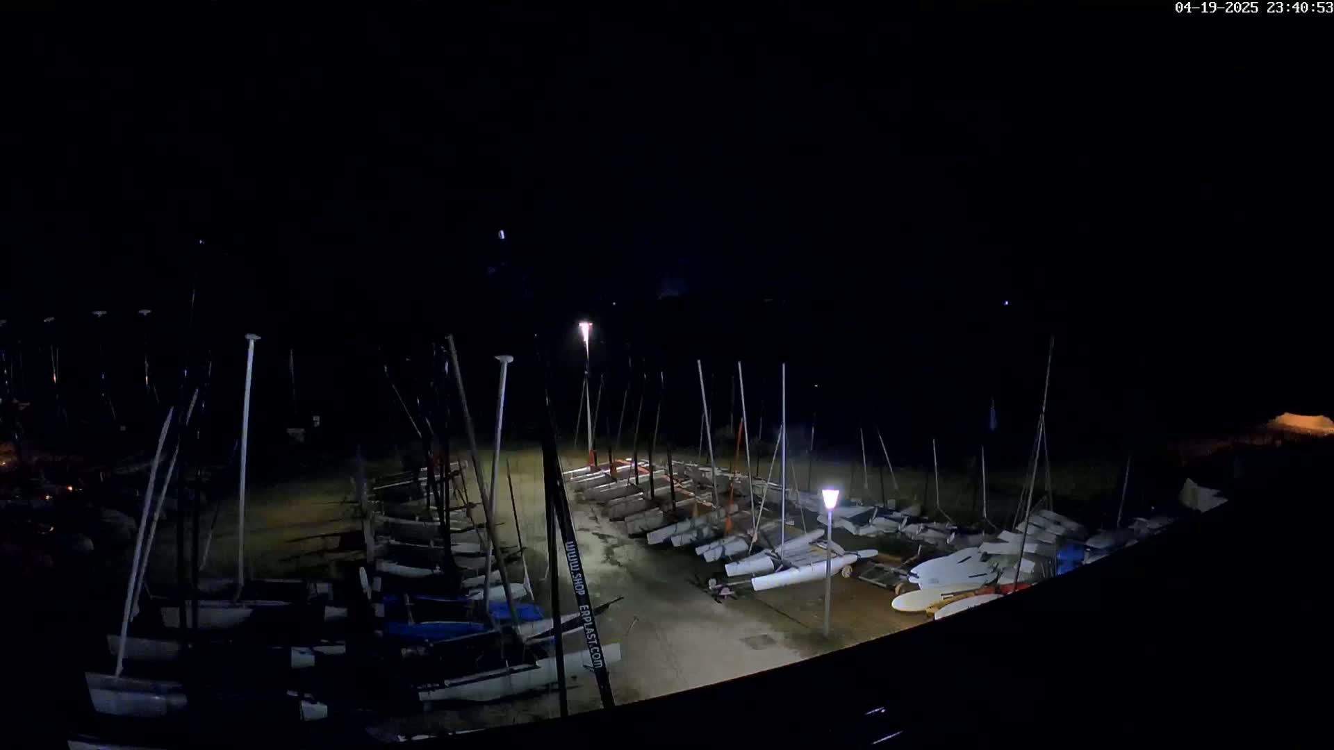 A nighttime, dimly lit view of numerous sailboats stored upright on land.