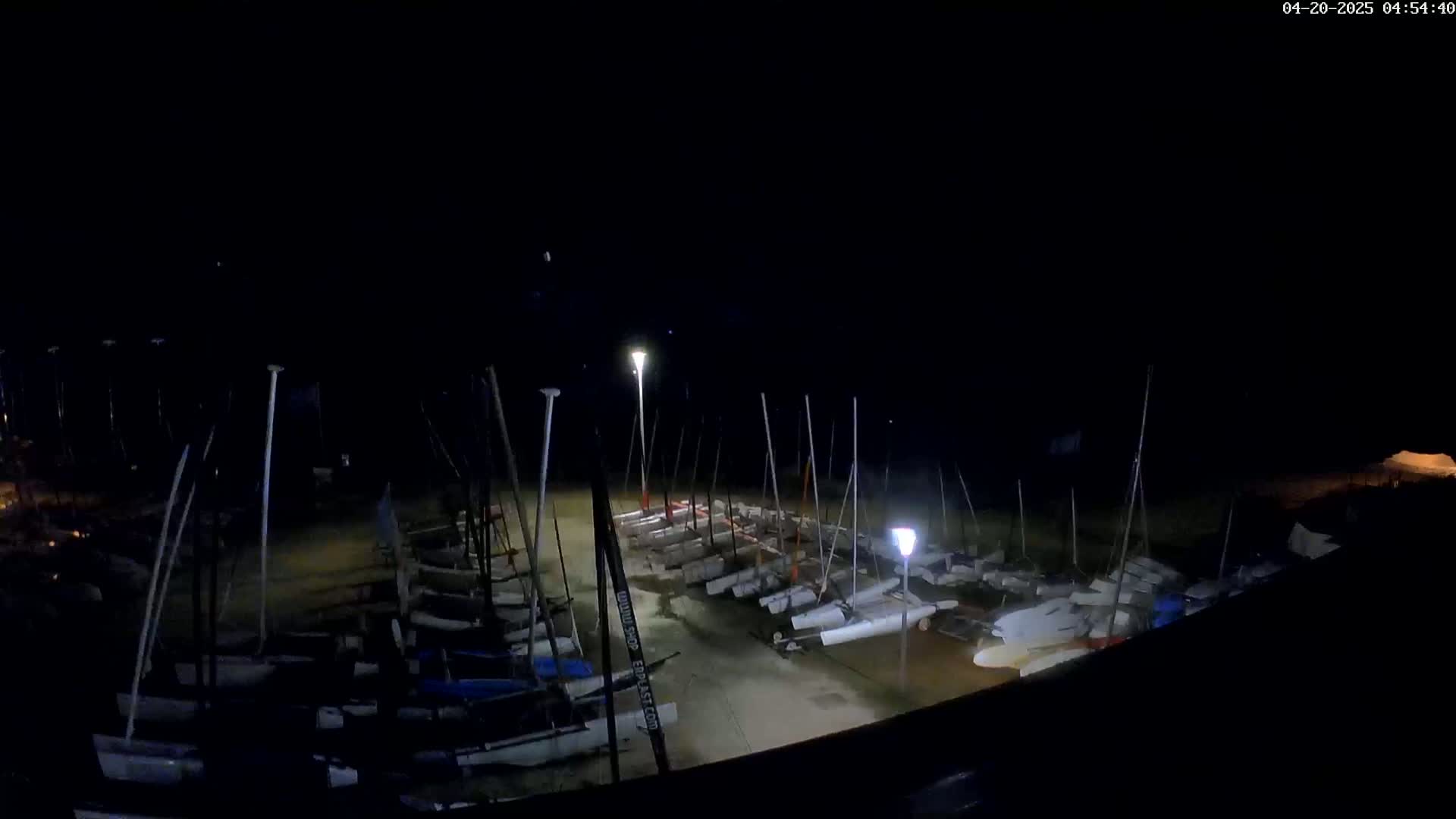 Many sailboats are docked at night under dim lighting.