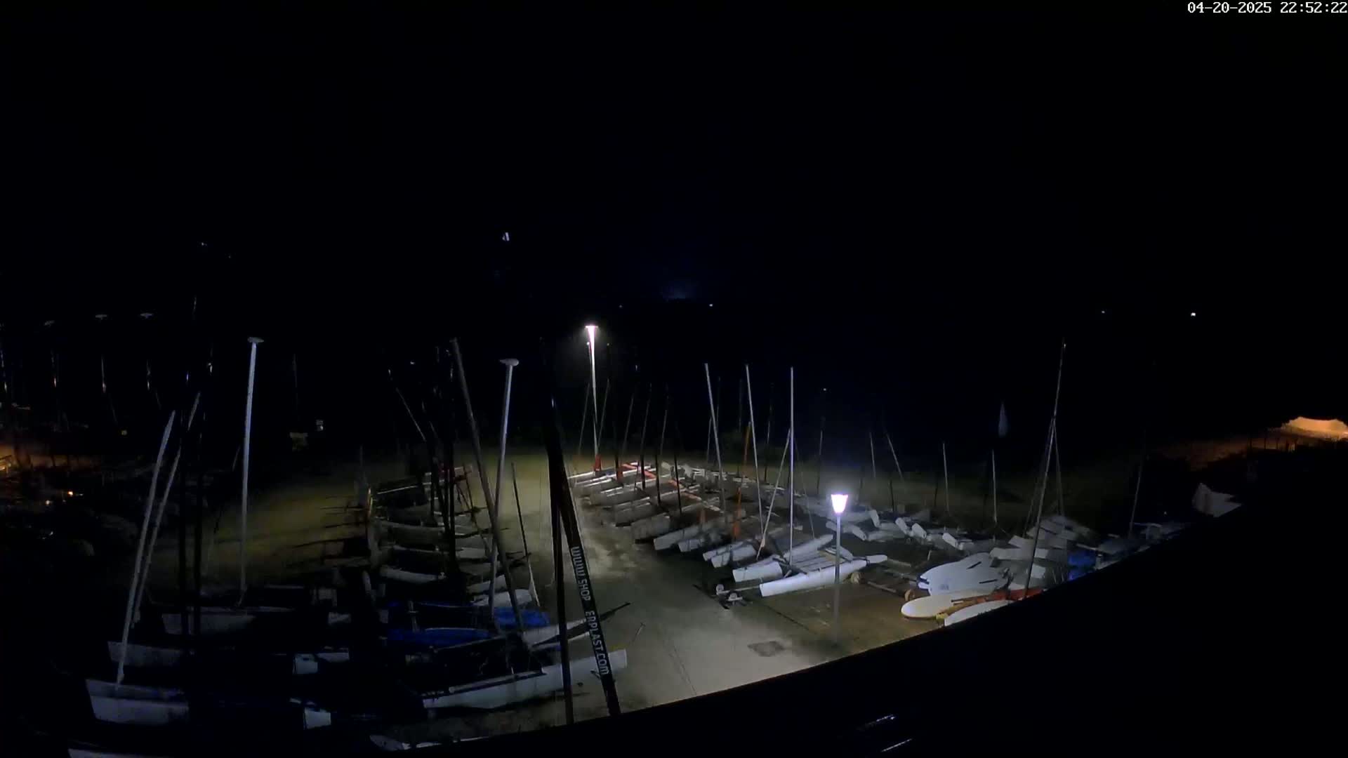A nighttime, dimly lit view of numerous sailboats docked in a row on a flat surface.