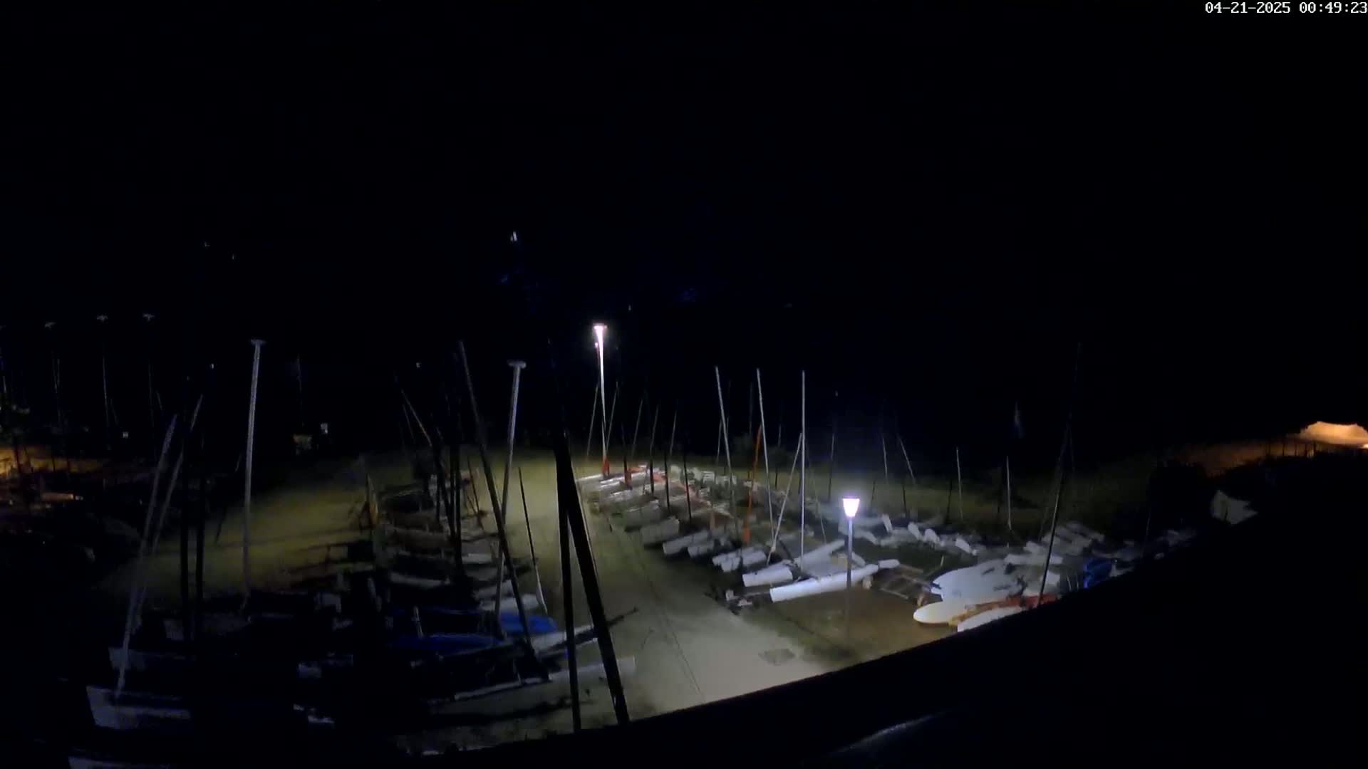 A nighttime view of numerous sailboats docked in a harbor, illuminated by several lights.