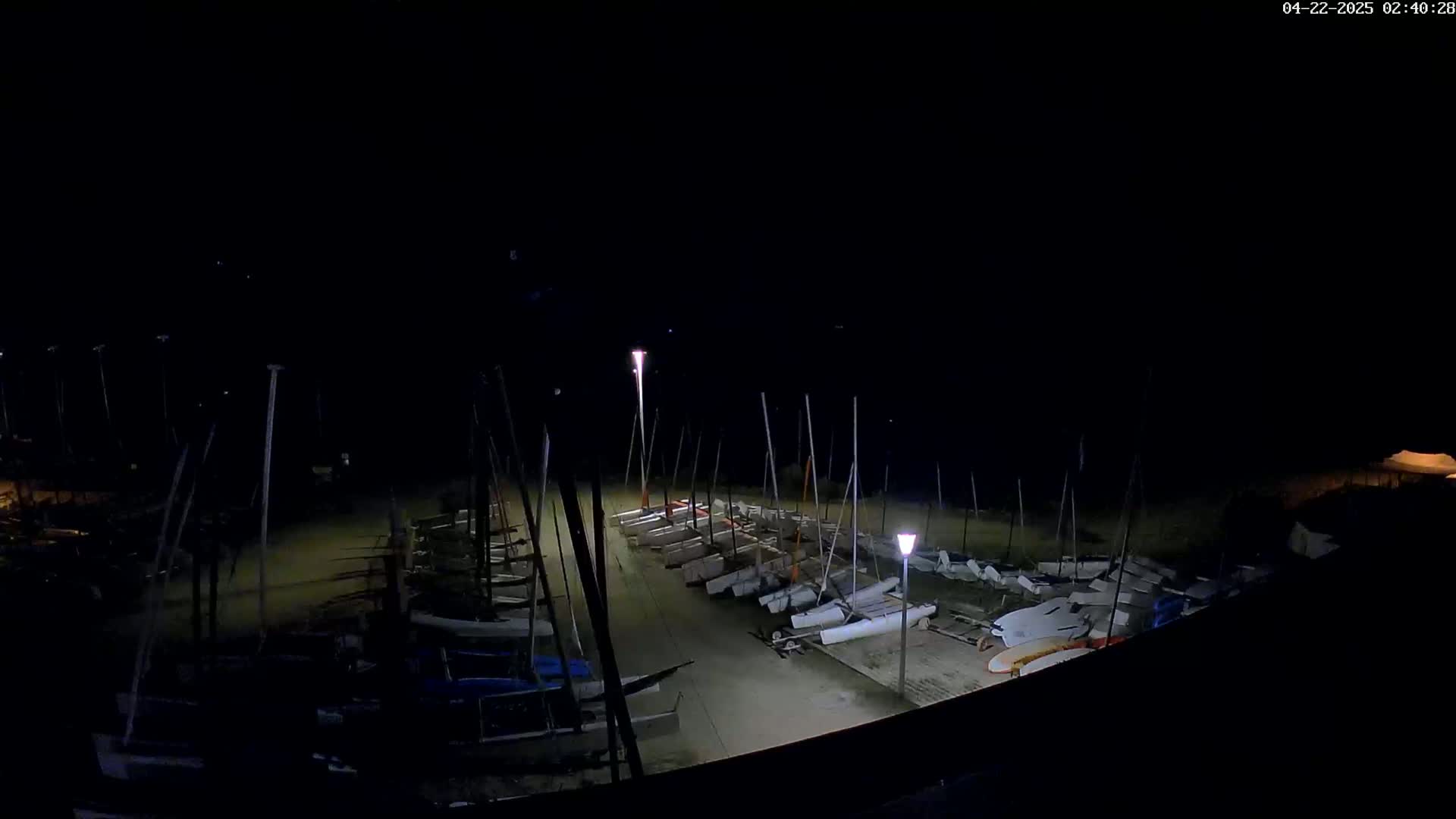 A nighttime view of numerous sailboats docked at a marina, illuminated by several lights.