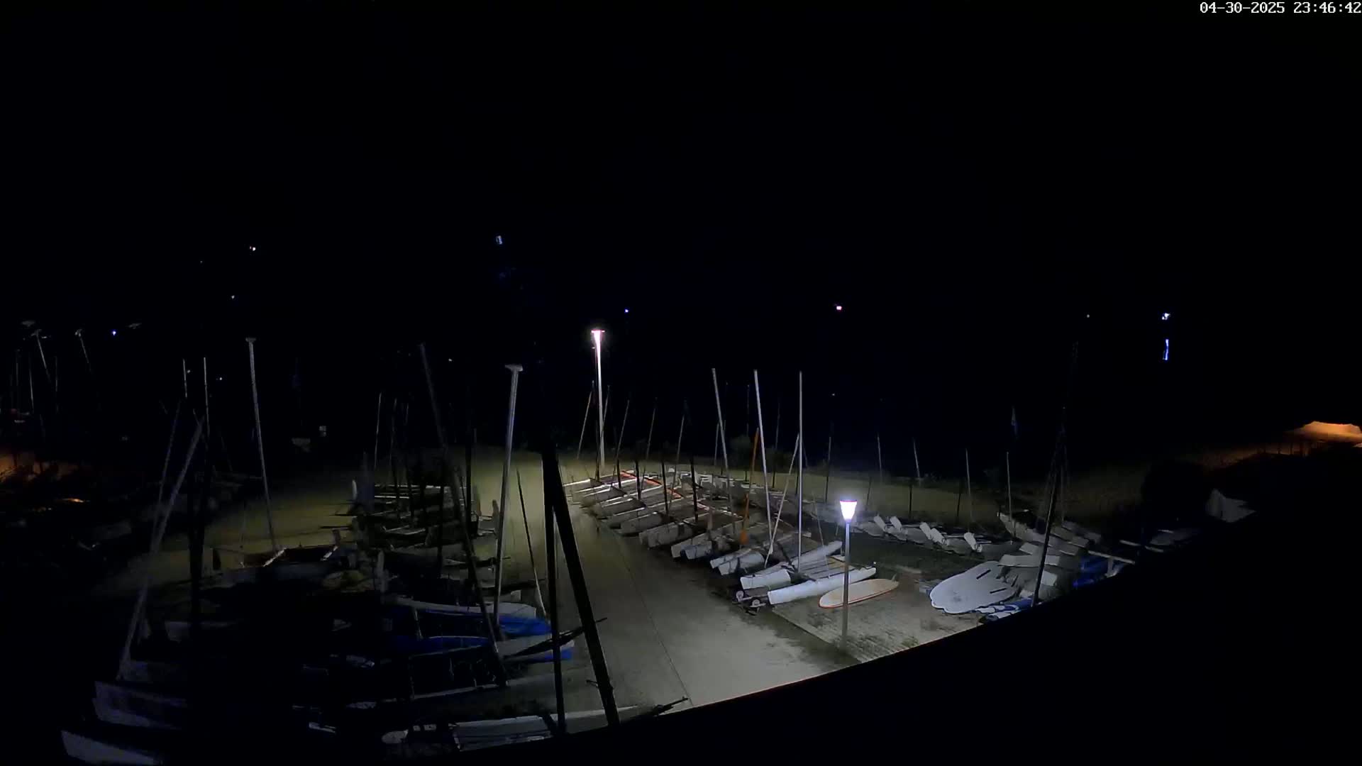 A nighttime view of numerous sailboats docked in a marina under a dark sky illuminated by several lights.