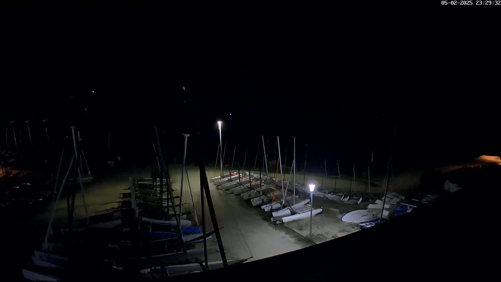 Numerous sailboats are docked at night under dimly lit conditions.