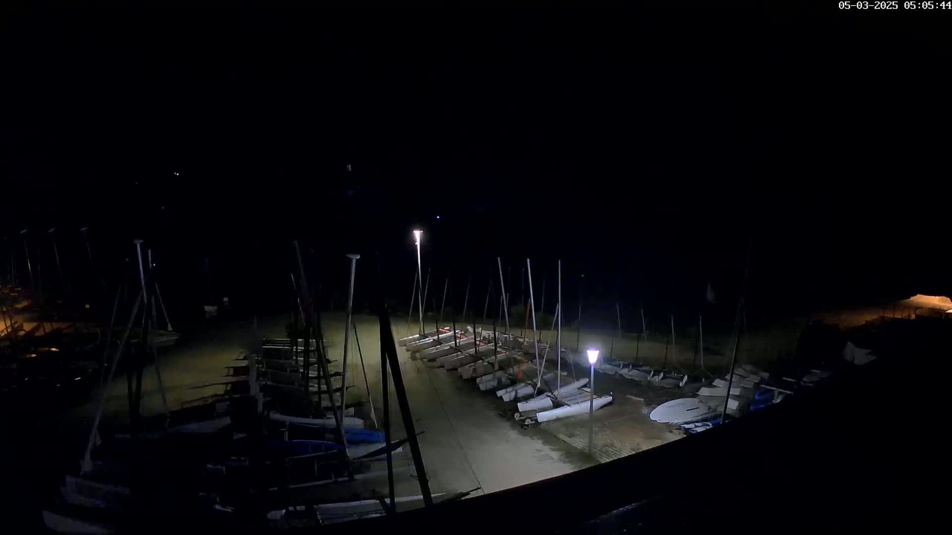 Many sailboats are docked at night under a dark sky illuminated by several lights.