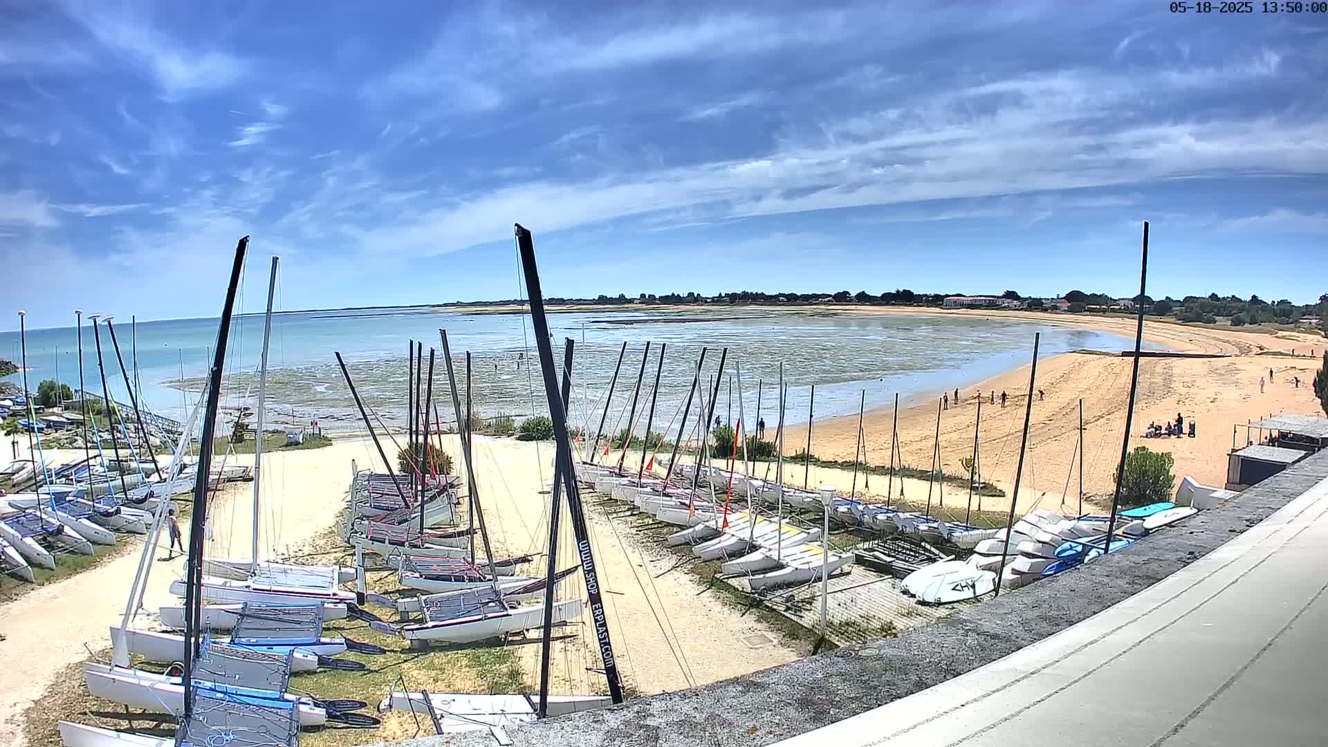 A sandy beach with numerous sailboats docked on a sunny day with a partly cloudy sky.