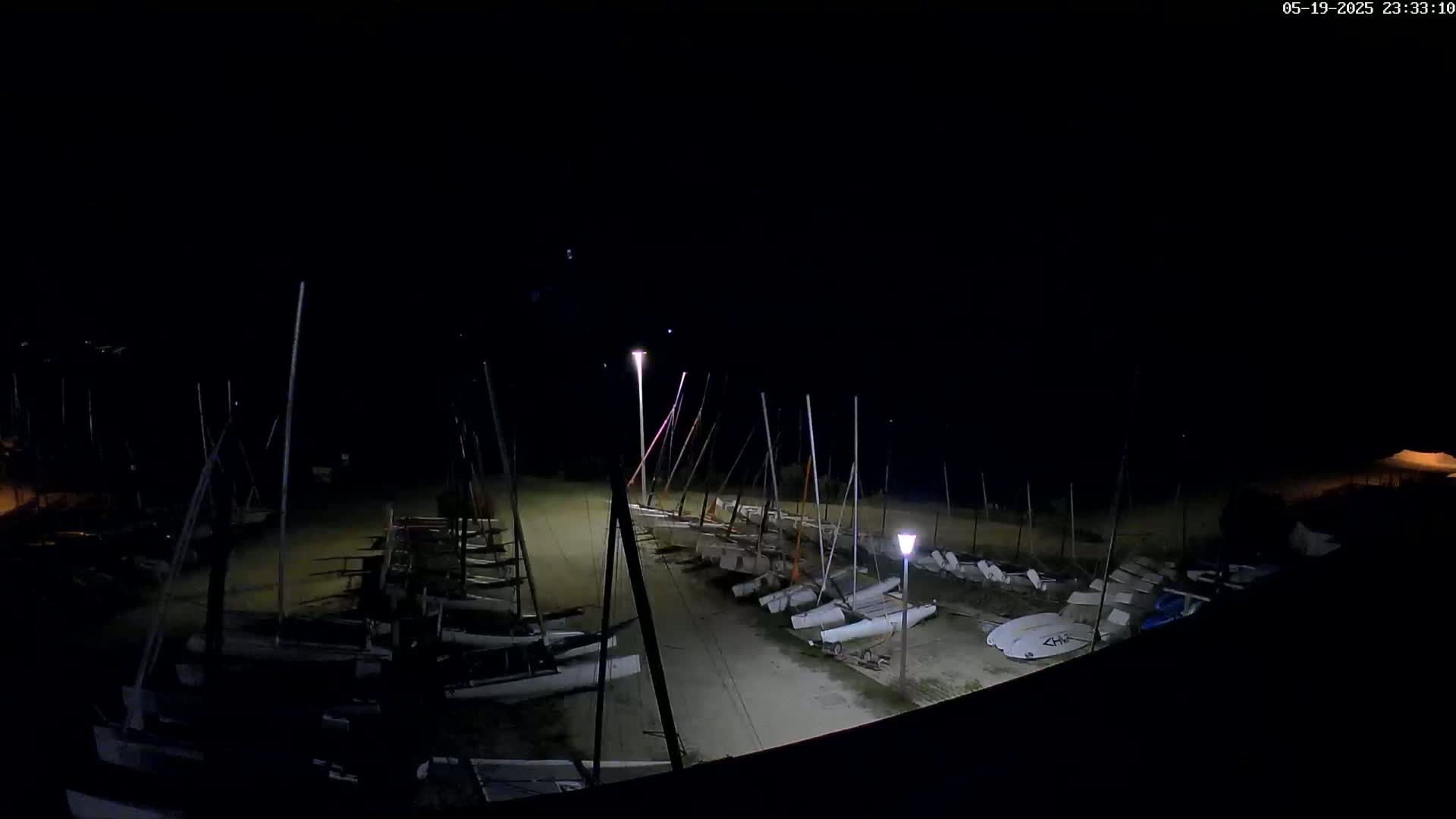 Numerous sailboats are parked on a beach at night under dimly lit conditions.