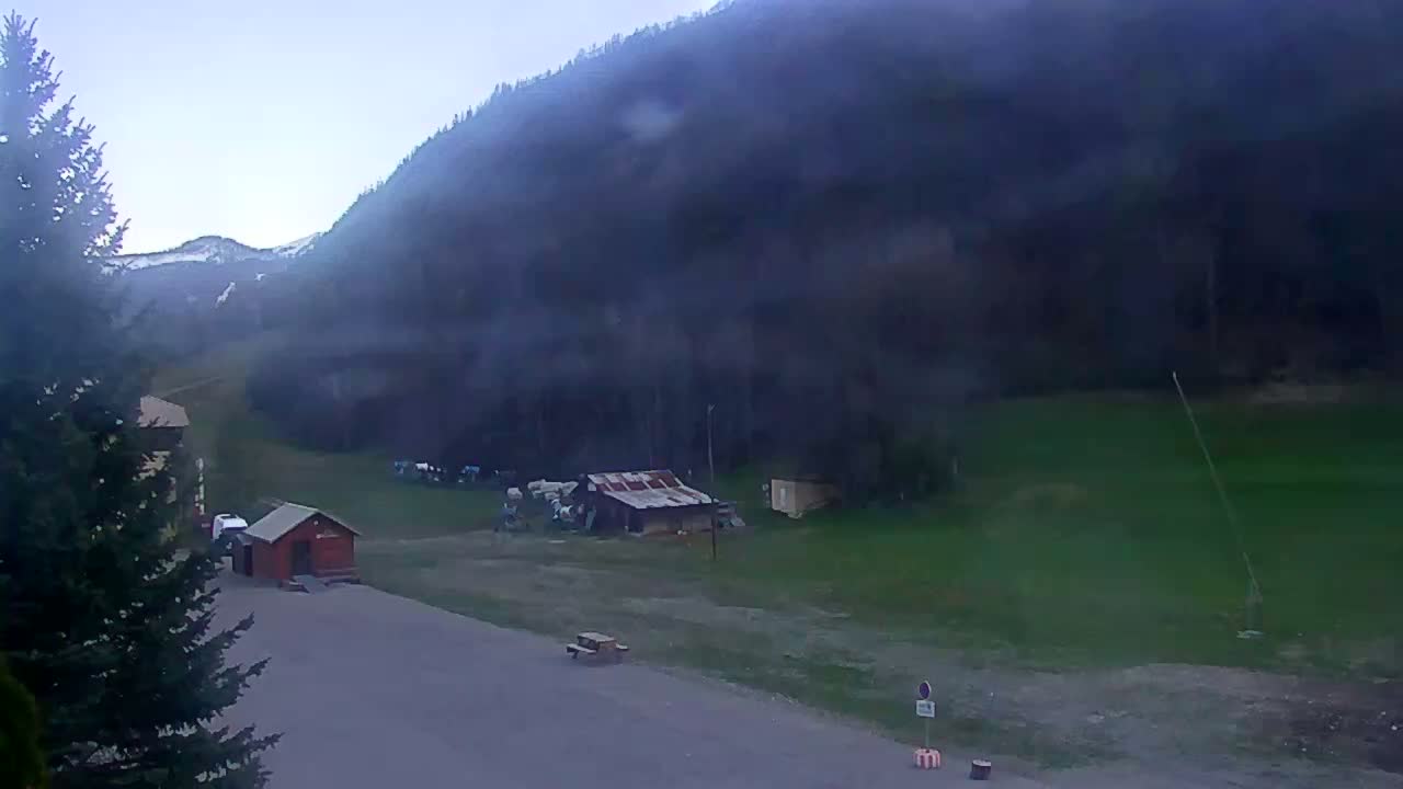 A hazy, overcast view shows a mountainside with sparse buildings and a small parking area near a forested hillside.