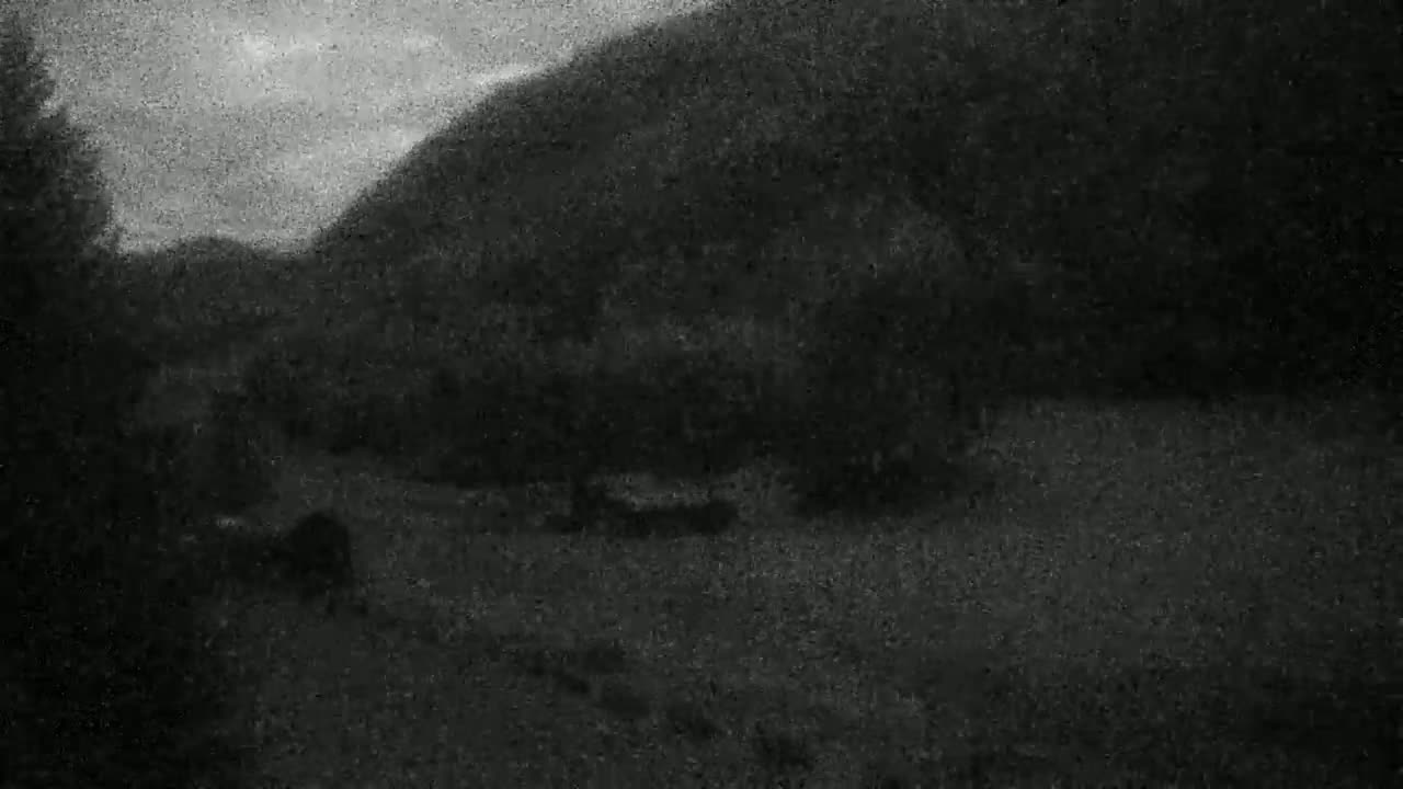 A low-light, grainy image shows a dark, possibly overcast landscape with a large hill or mountain in the background and some indistinct objects in the foreground.