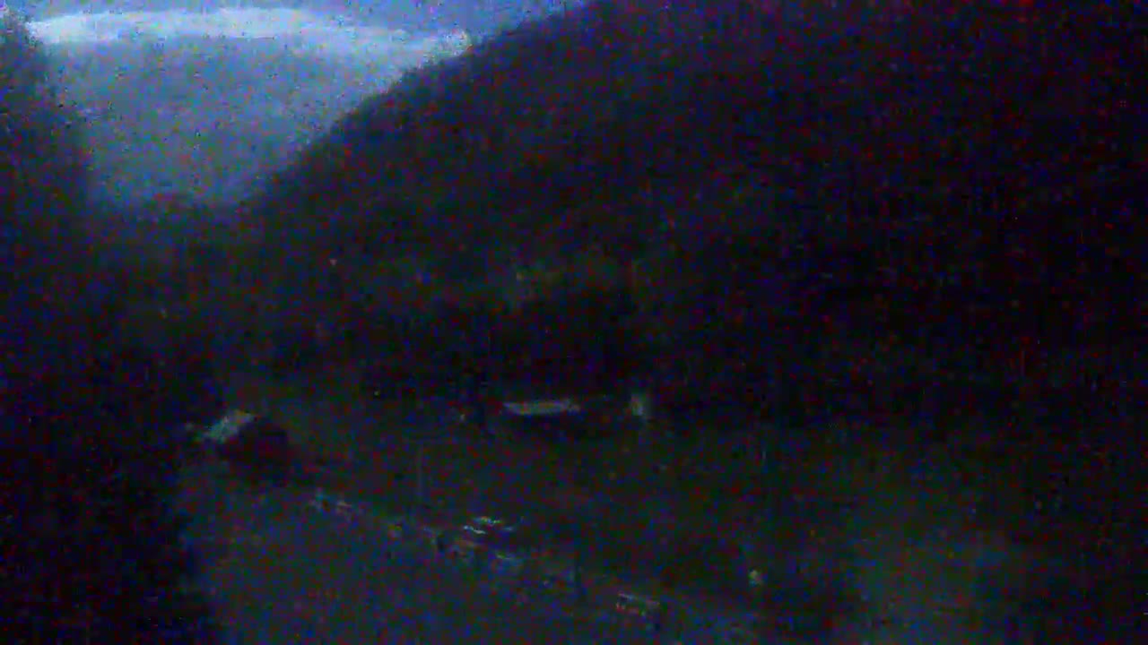 A dark, blurry image shows a road with vehicles at night under an overcast sky, near a dark mountainside.