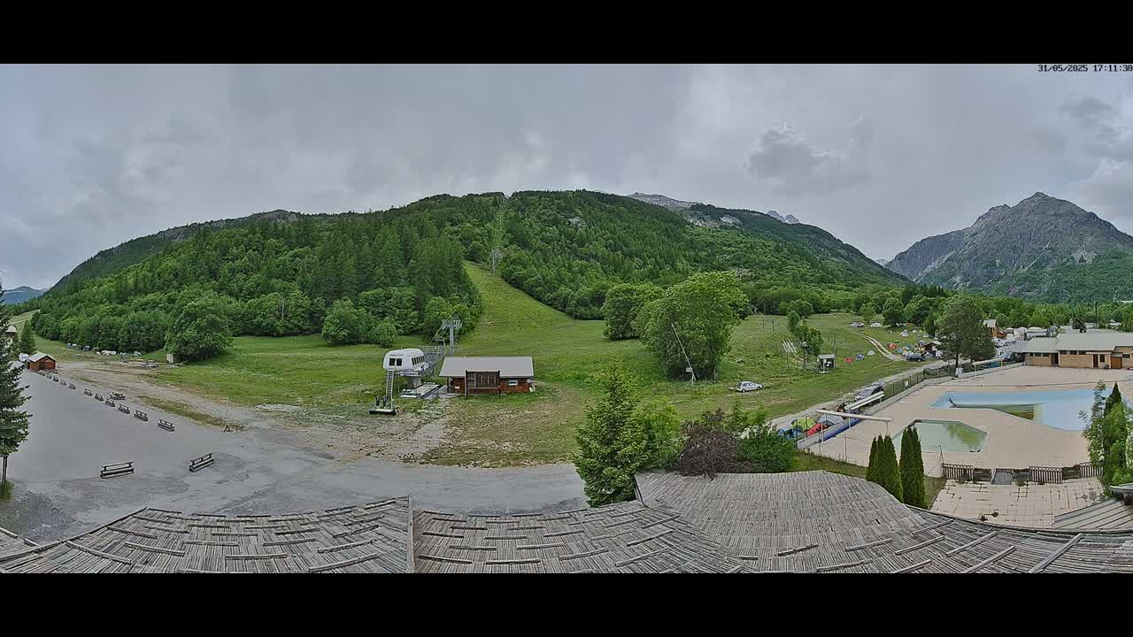 A panoramic view shows a mountainous region with a ski lift, a small building, a swimming pool, and an overcast sky.