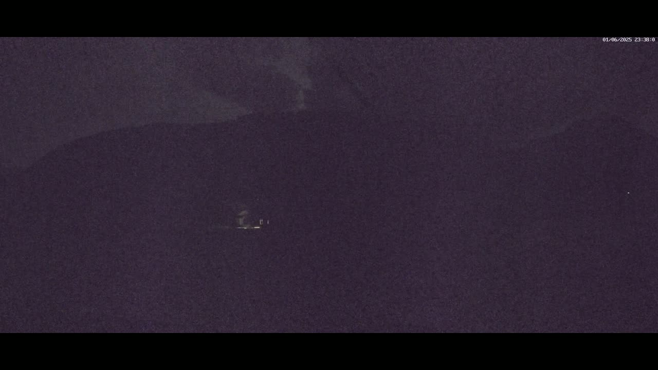 A dimly lit structure is visible against a dark, nighttime landscape under a cloudy sky.