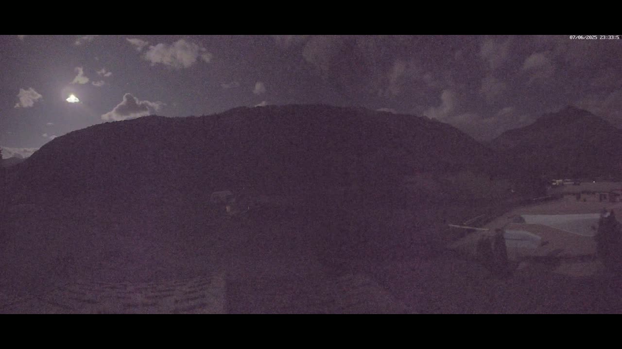 A nighttime, partly cloudy view shows a large, dark mountain silhouetted against a moonlit sky.