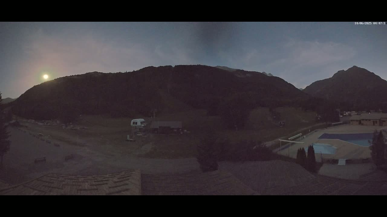 A low-light outdoor scene shows a mountainous landscape at dusk or dawn, with a swimming pool and buildings visible in the foreground.