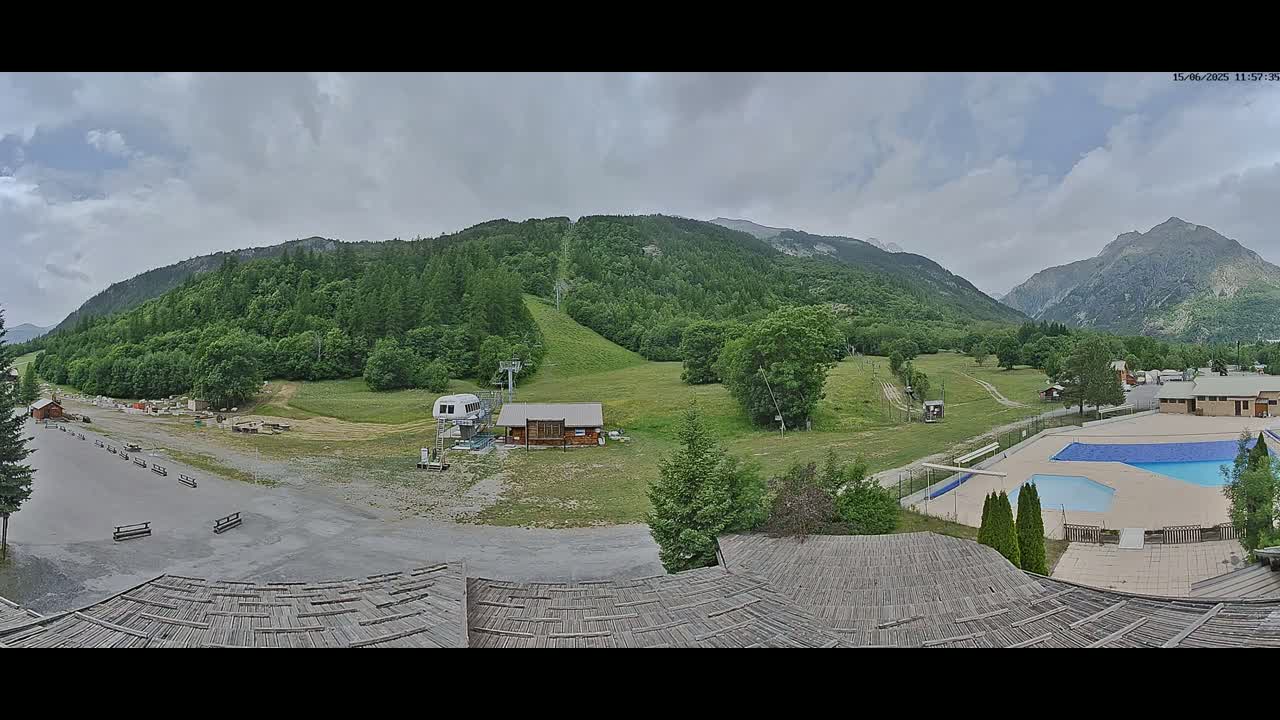 A mountain valley with a ski lift, a small building, an outdoor pool, and overcast skies.