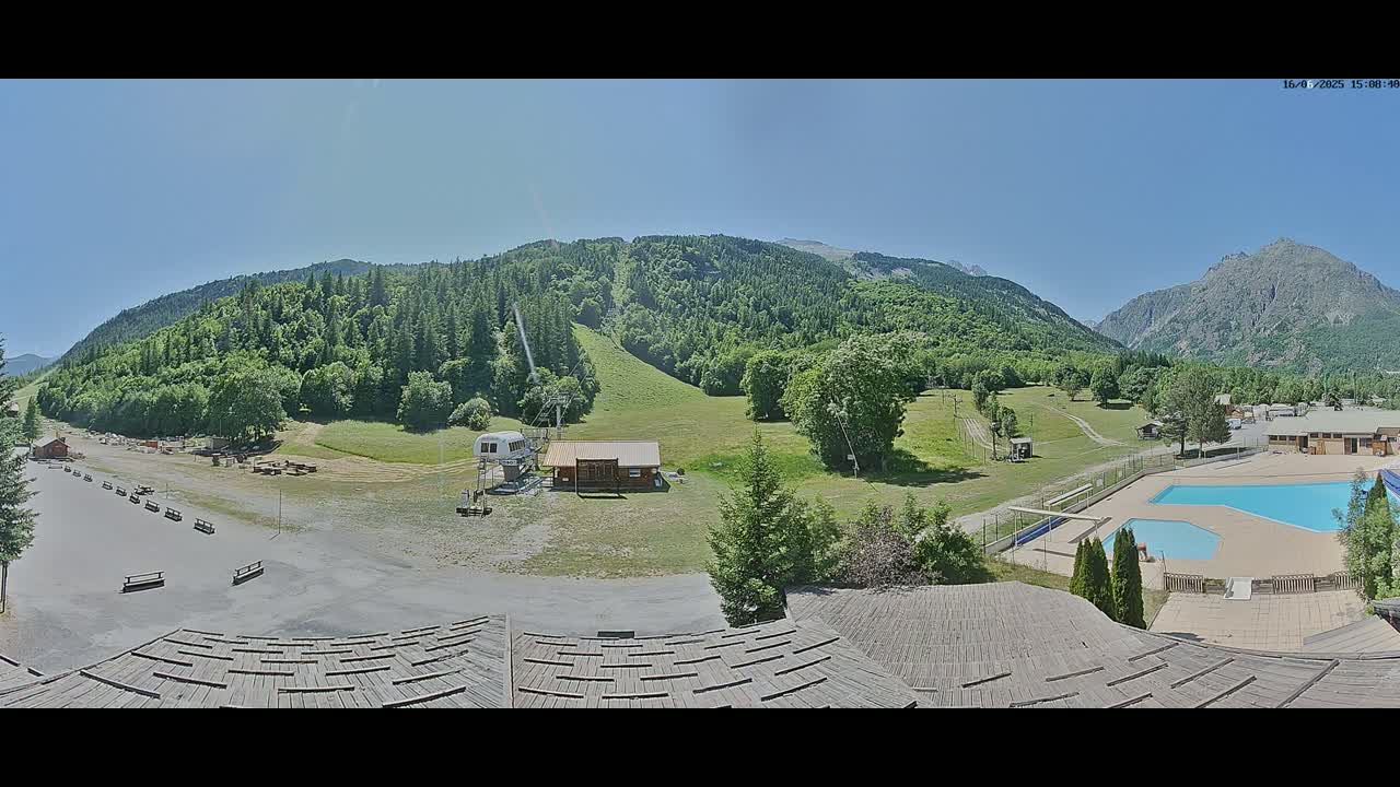 A panoramic view shows a sunny mountain valley with a ski lift, several buildings, and an outdoor swimming pool.