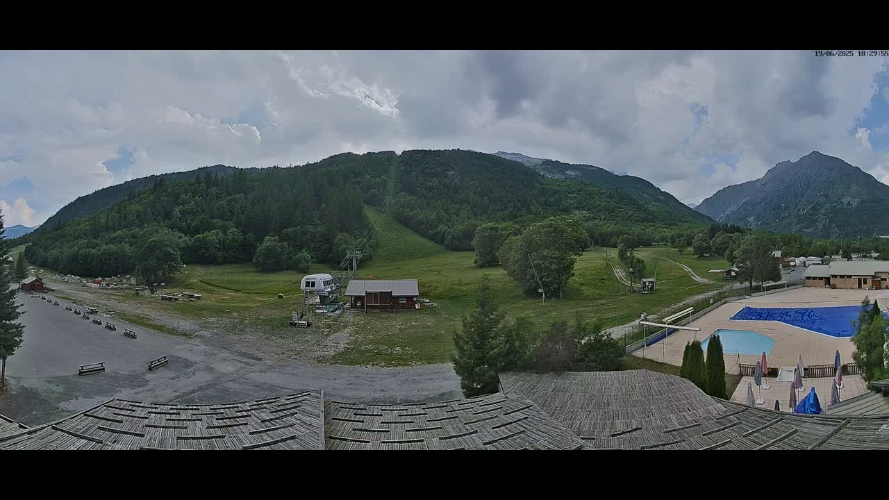 A mountain resort with a swimming pool and chairlift is visible under a partly cloudy sky.