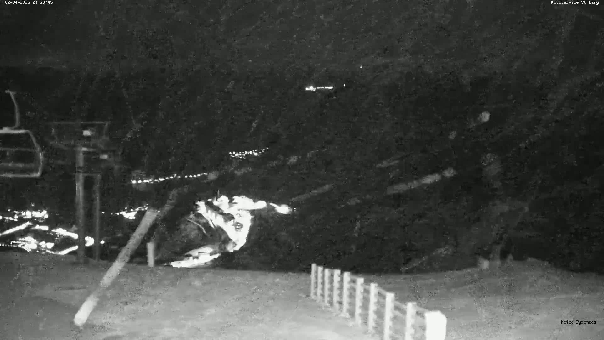 A nighttime, snowy scene shows a ski lift and a snow-covered slope with faint lights in the distance.