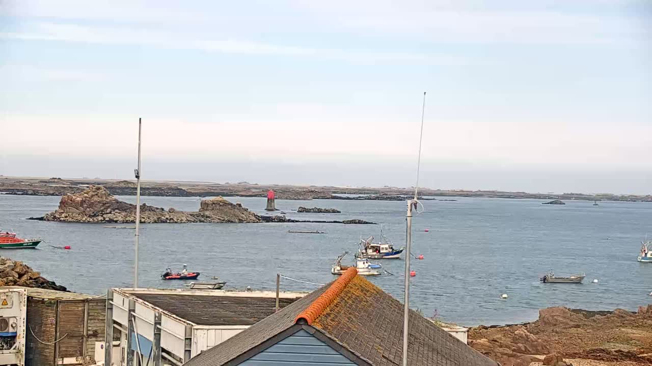 Several small boats are moored near rocky outcrops in calm water under an overcast sky.
