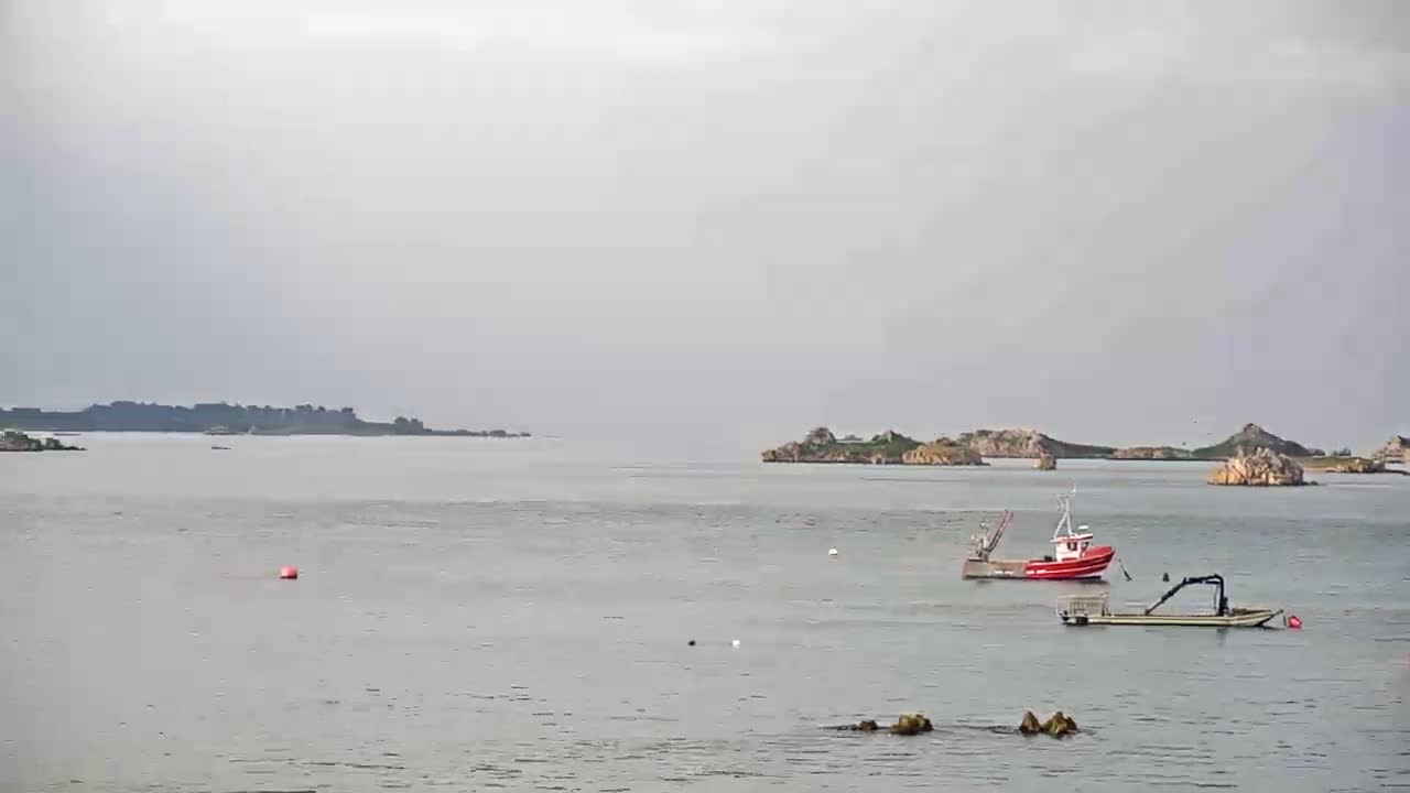 Two small fishing boats are moored in calm, gray water near several small, rocky islands under an overcast sky.