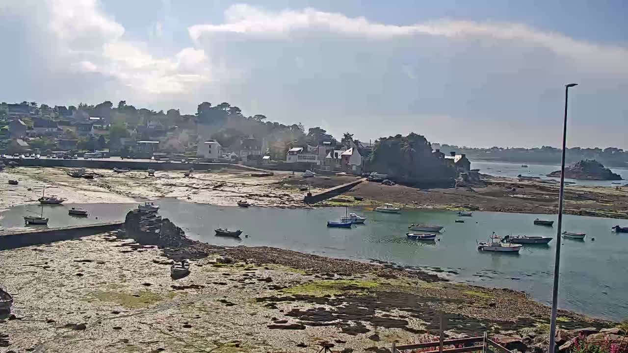 A small coastal town with several boats in a harbor at low tide under a partly cloudy sky.