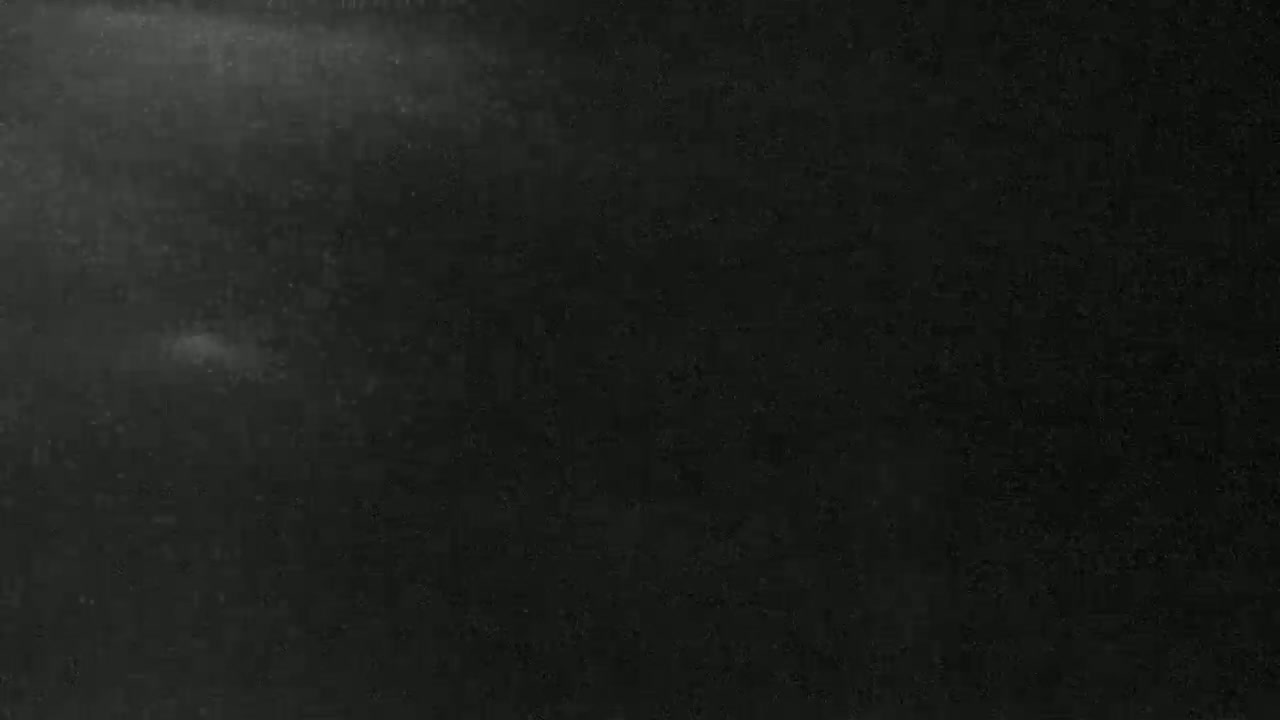 A dark, possibly nighttime, image shows a mostly black background with subtle variations in shading and faint, light specks.