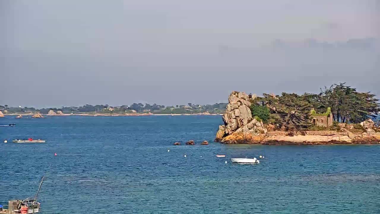 A small, rocky island with trees and a stone structure is visible in a calm, blue body of water, under a hazy sky.