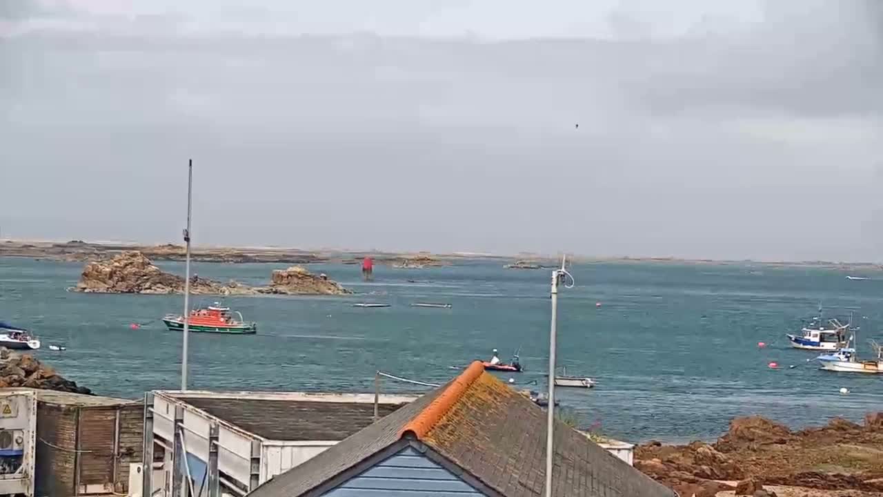 Several boats are in a calm body of water near rocky outcrops under an overcast sky.