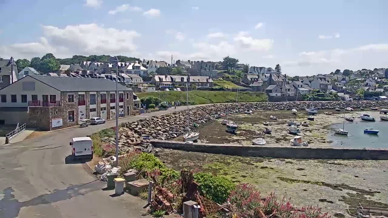 A sunny day reveals a small harbor filled with boats at low tide, nestled beside a town built on a hillside.