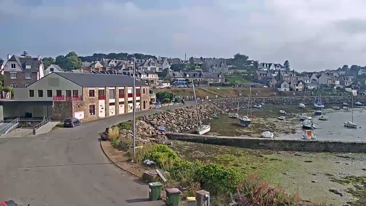 A small coastal town with a harbor filled with sailboats is visible under partly cloudy skies.