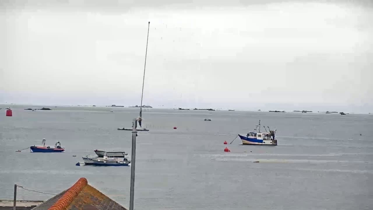 Several small boats are moored in a calm, gray sea under an overcast sky.