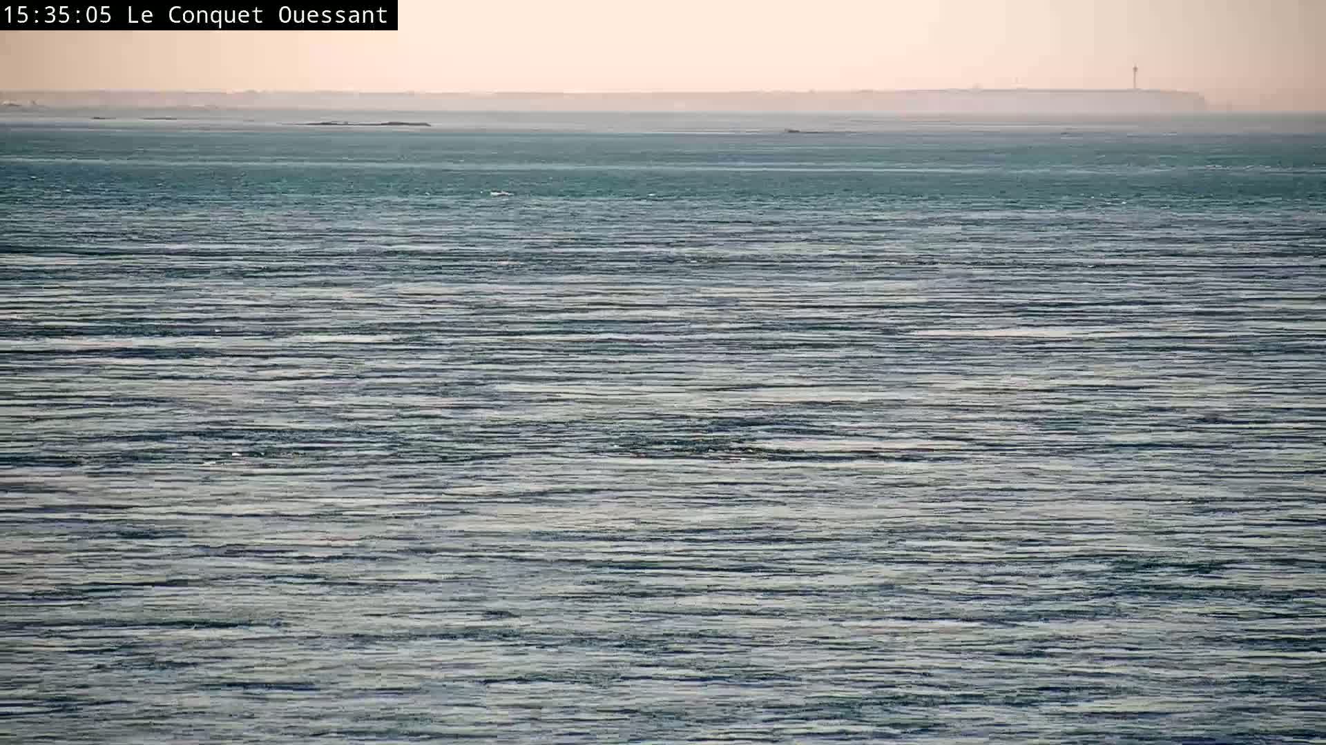 A calm, teal ocean stretches to a hazy, distant landmass under a pale sky.