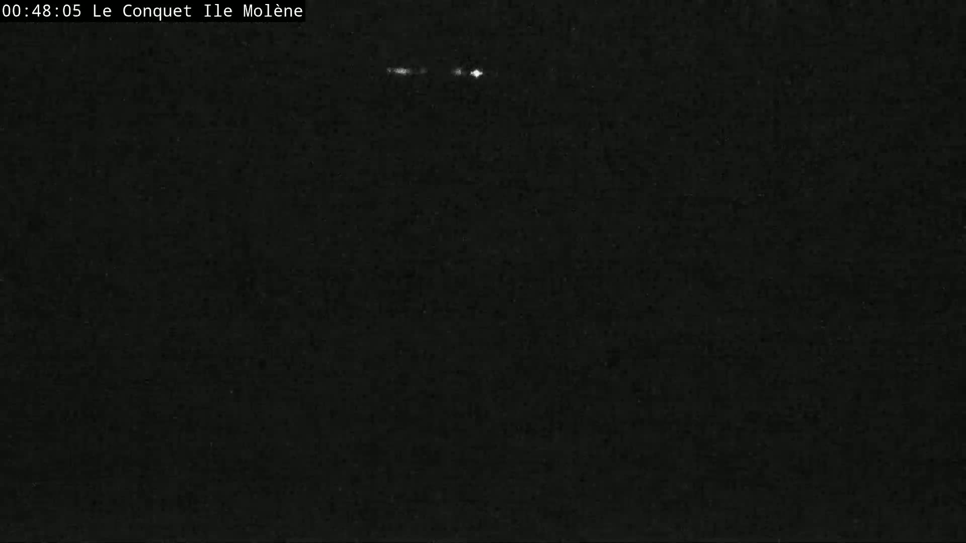 A dark, nighttime image shows a few faint lights in the distance.