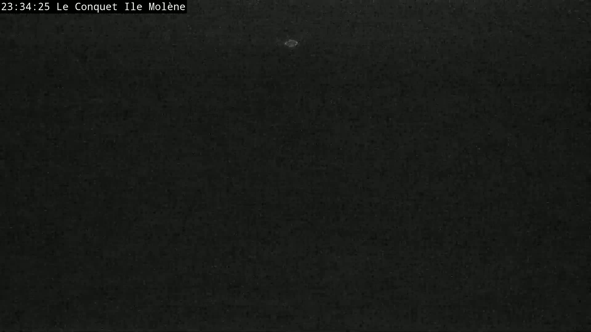A dark, grainy image shows a mostly black, nighttime scene with a single, small, bright spot near the center.