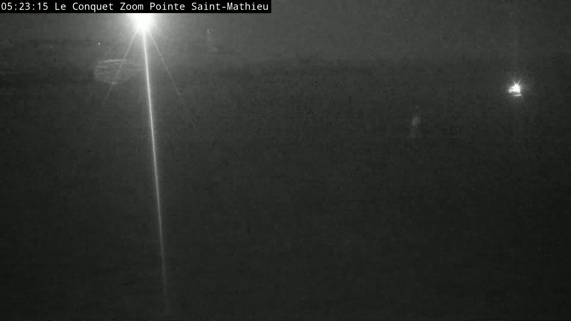 A nighttime, low-light image shows a bright light source in the center, with faint lights visible in the distance.