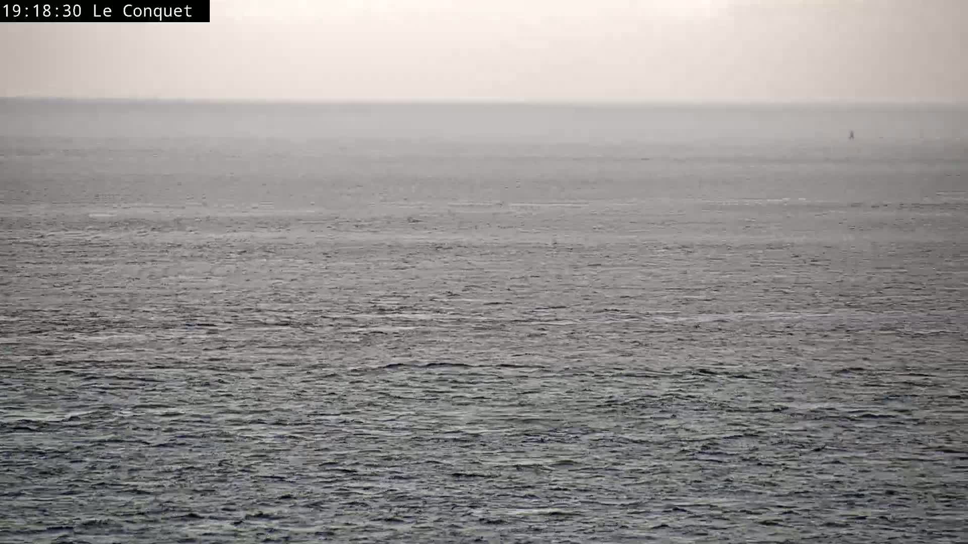 A hazy, overcast day shows a calm, gray sea with a small, distant object on the horizon.