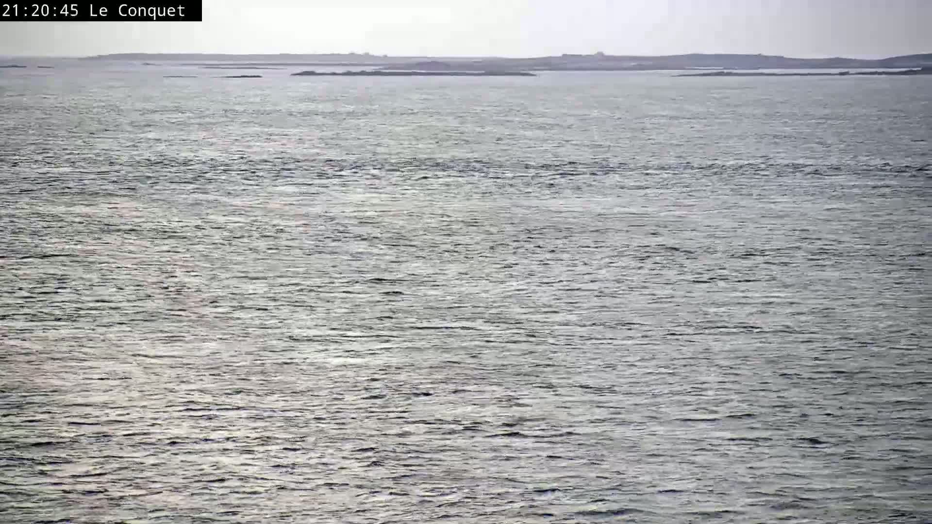 A calm, gray sea stretches to a distant, low-lying landmass under an overcast sky.
