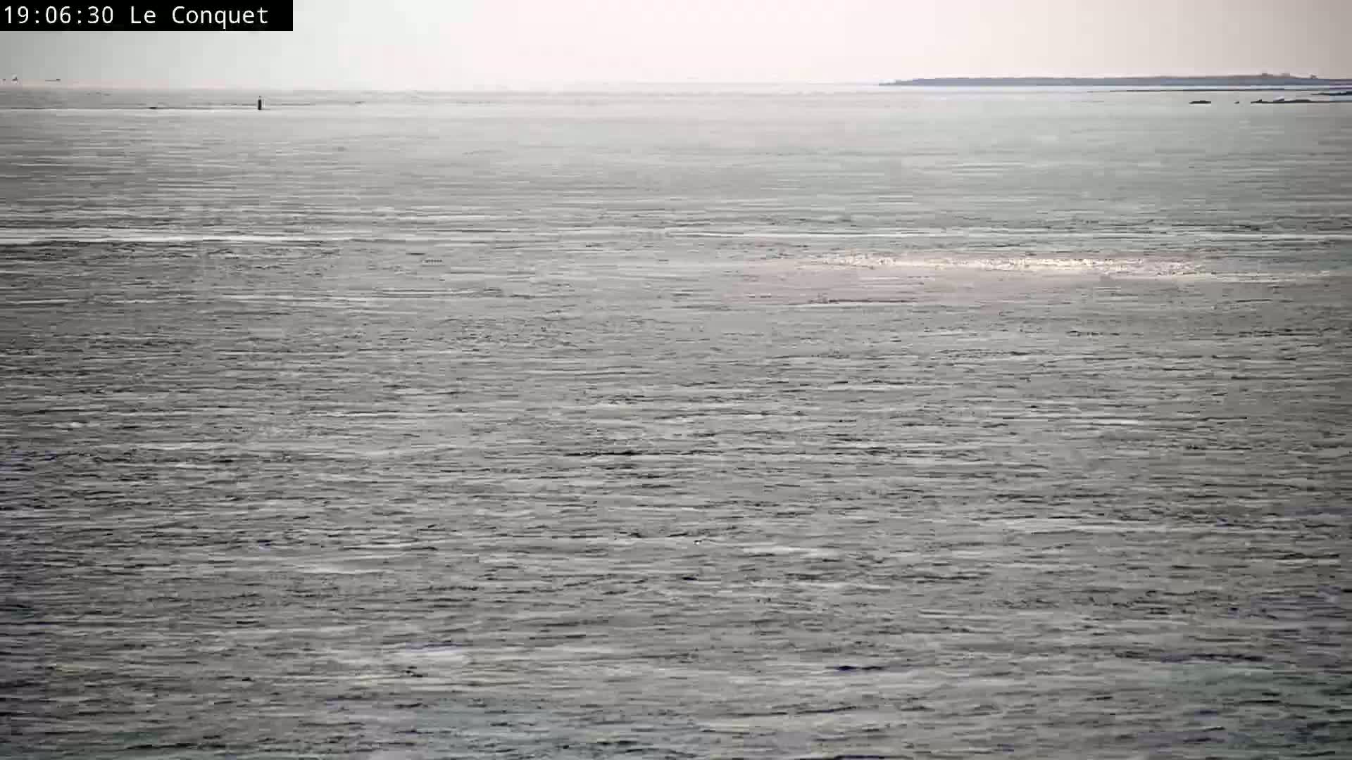A calm, gray sea stretches to a distant, low-lying landmass under a cloudy sky.