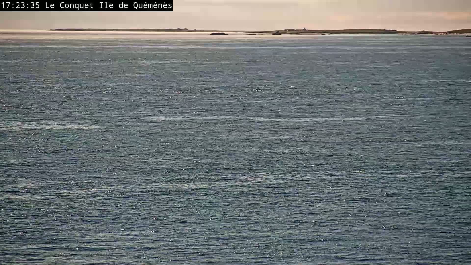 A calm, expansive body of water shows a distant, low-lying landmass under a mostly clear sky.