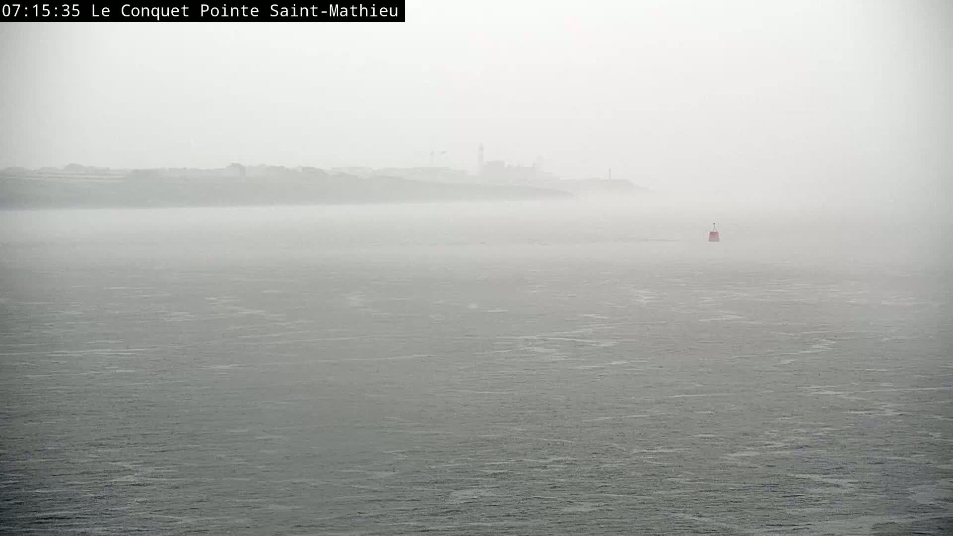 A hazy, gray body of water stretches to a distant, indistinct shoreline under a foggy sky.
