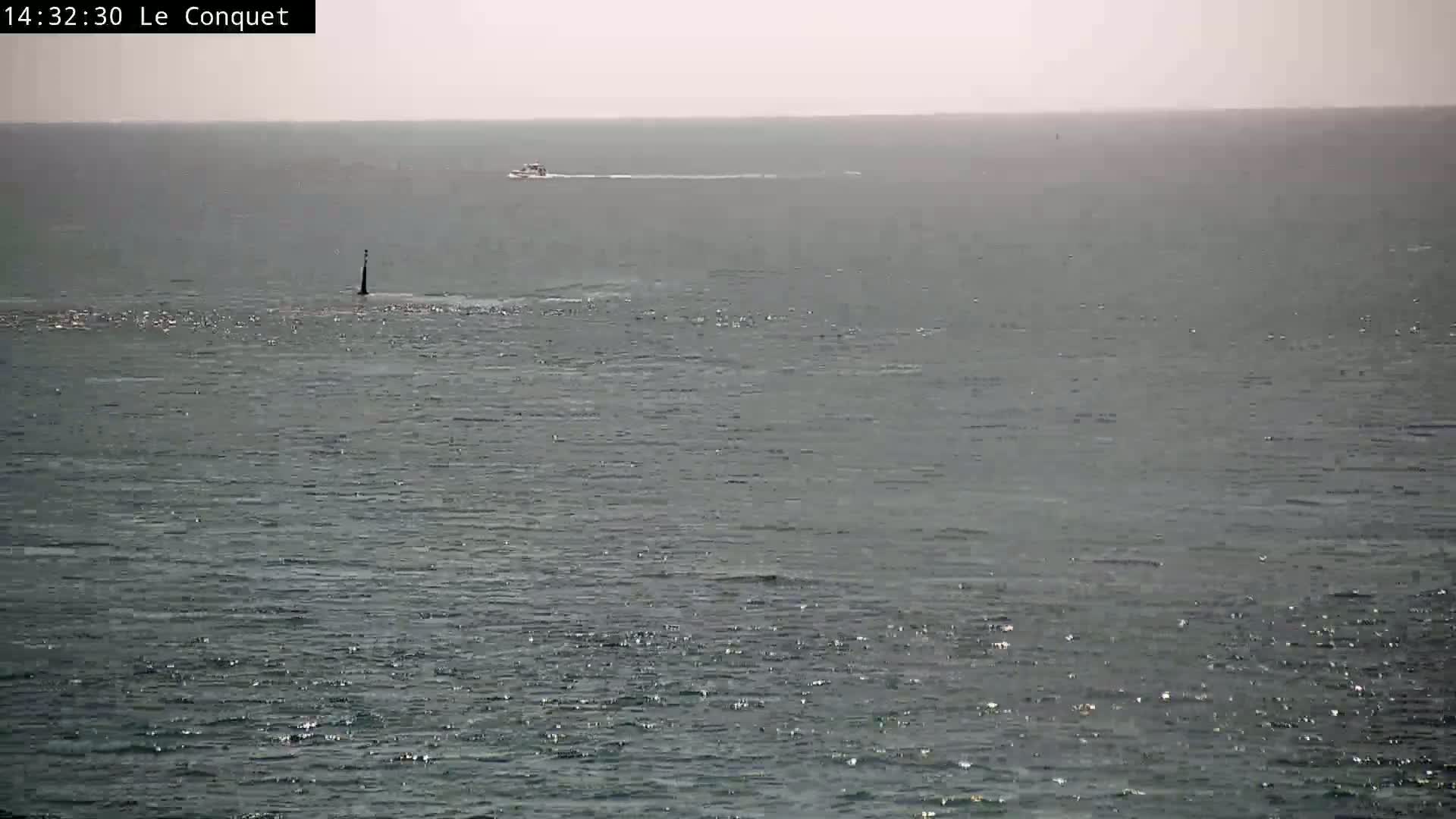 A boat travels across a calm, gray sea with a single marker post in the water.