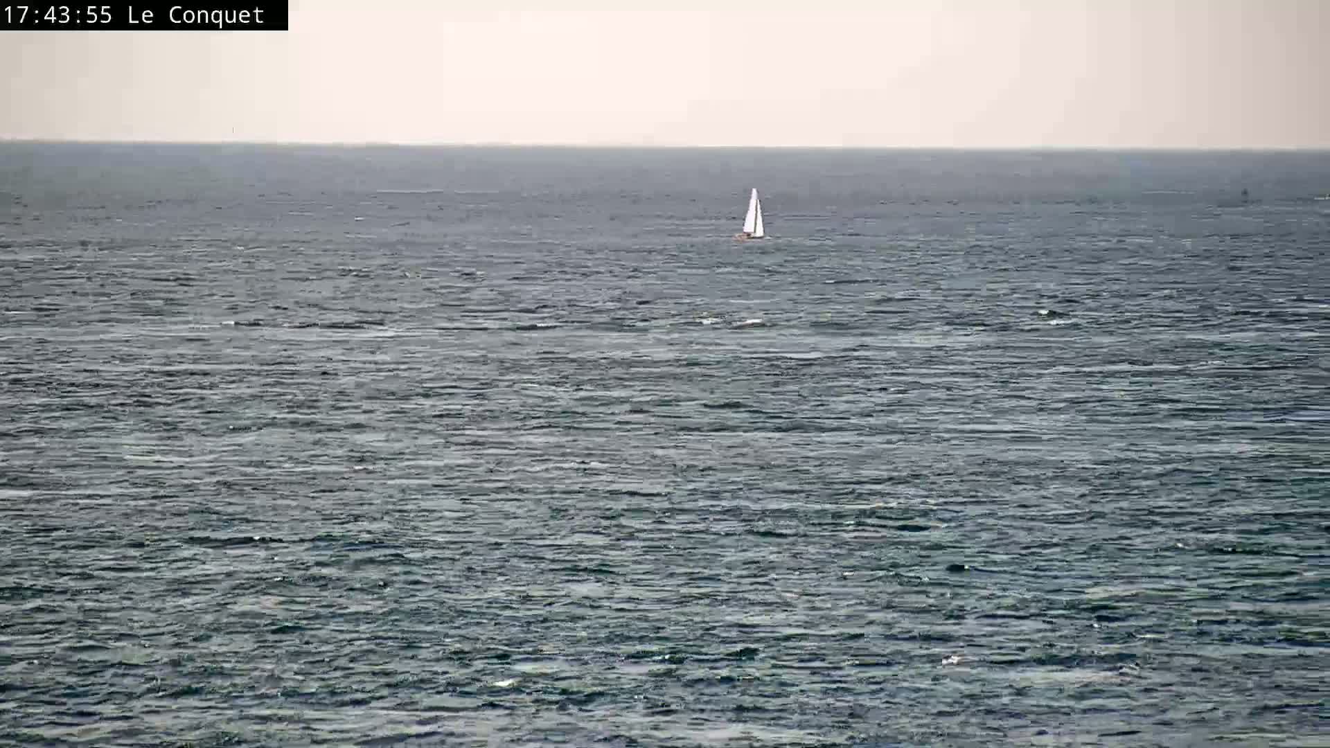 A single sailboat is visible on a calm, gray-toned sea under a cloudy sky.